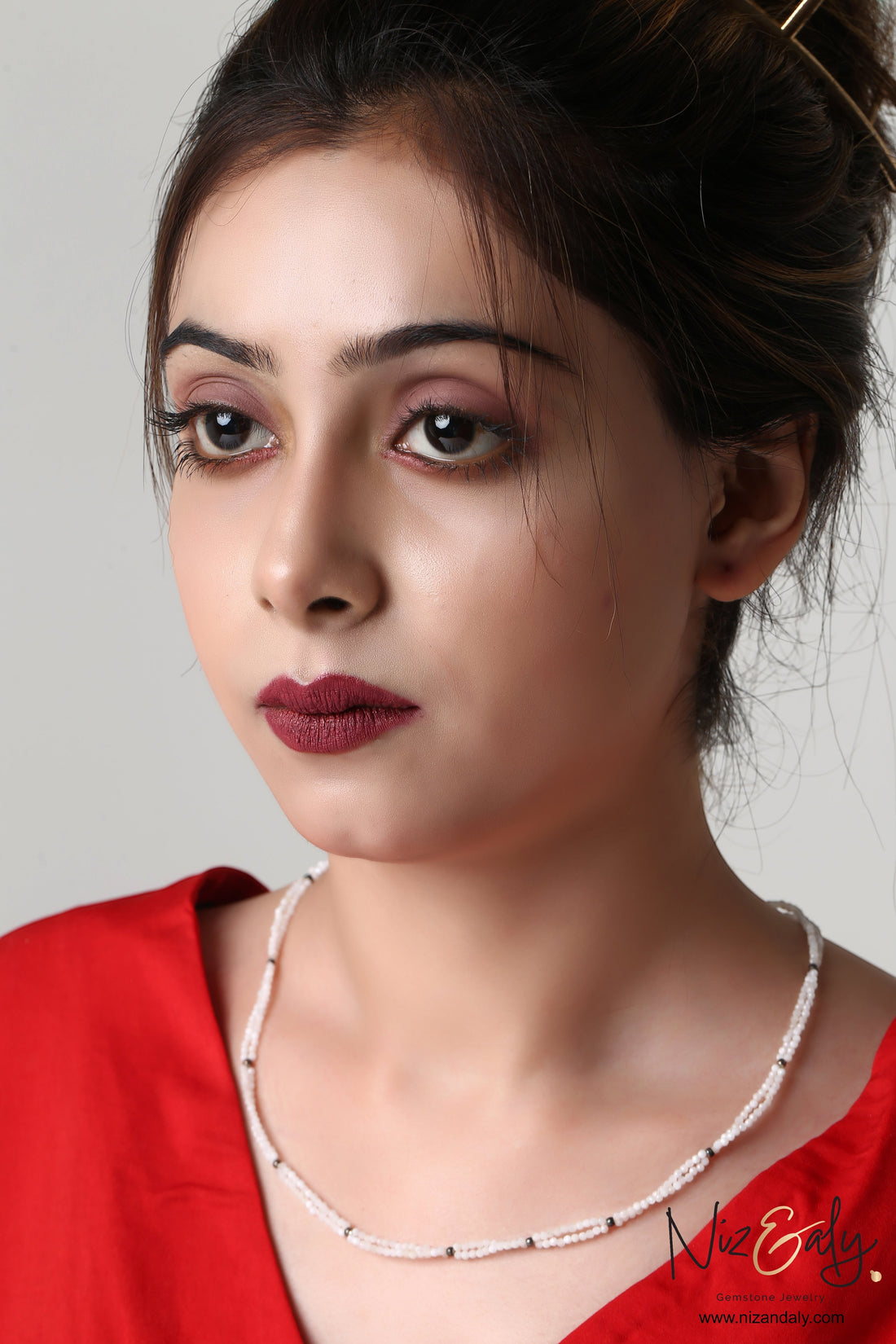 Niz & Aly dainty double-strand milky quartz necklace worn by a woman in a red top, featuring delicate white beads.
