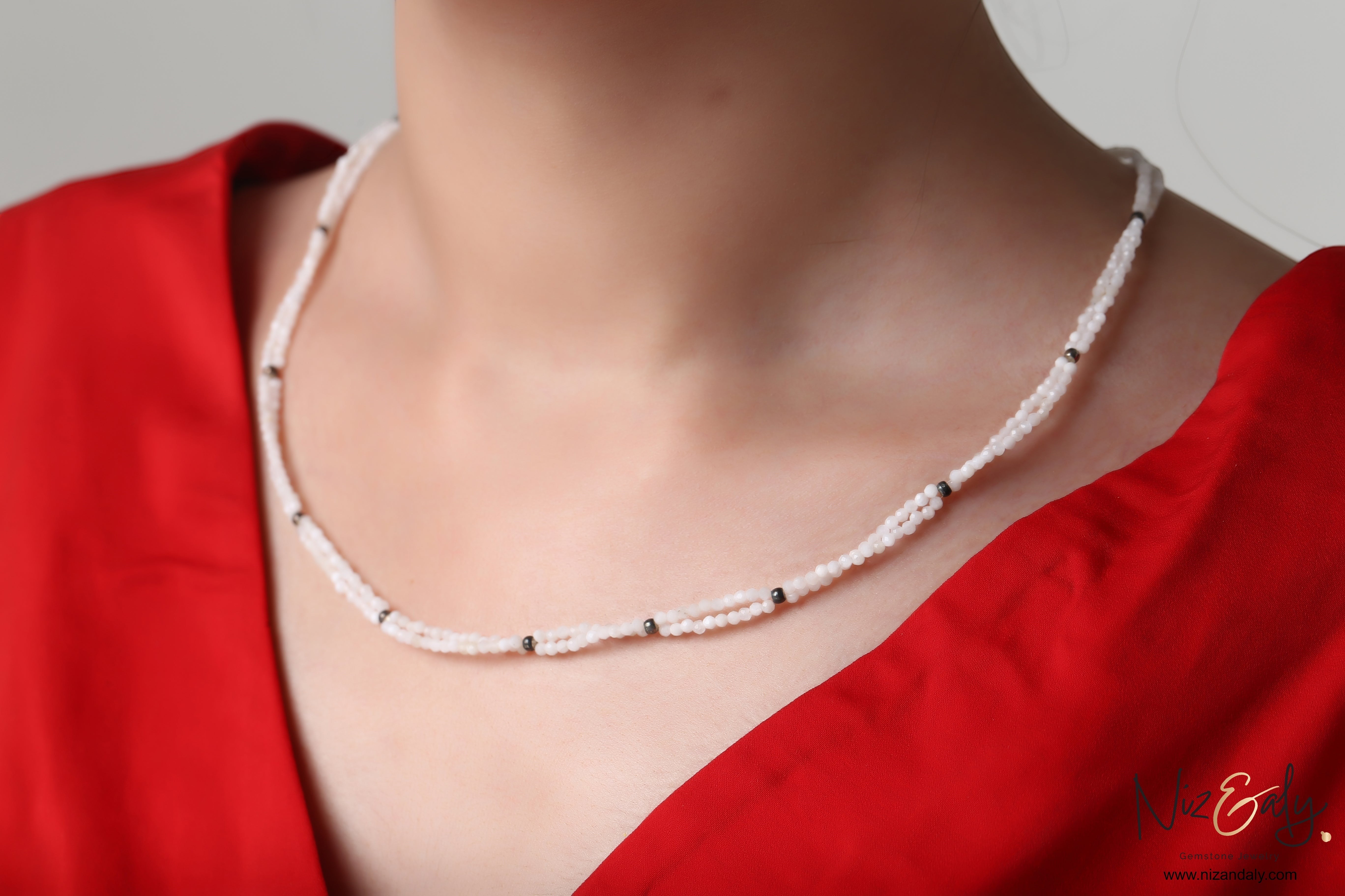 Niz & Aly dainty double-strand necklace featuring small milky quartz beads with dark accents worn on a red top