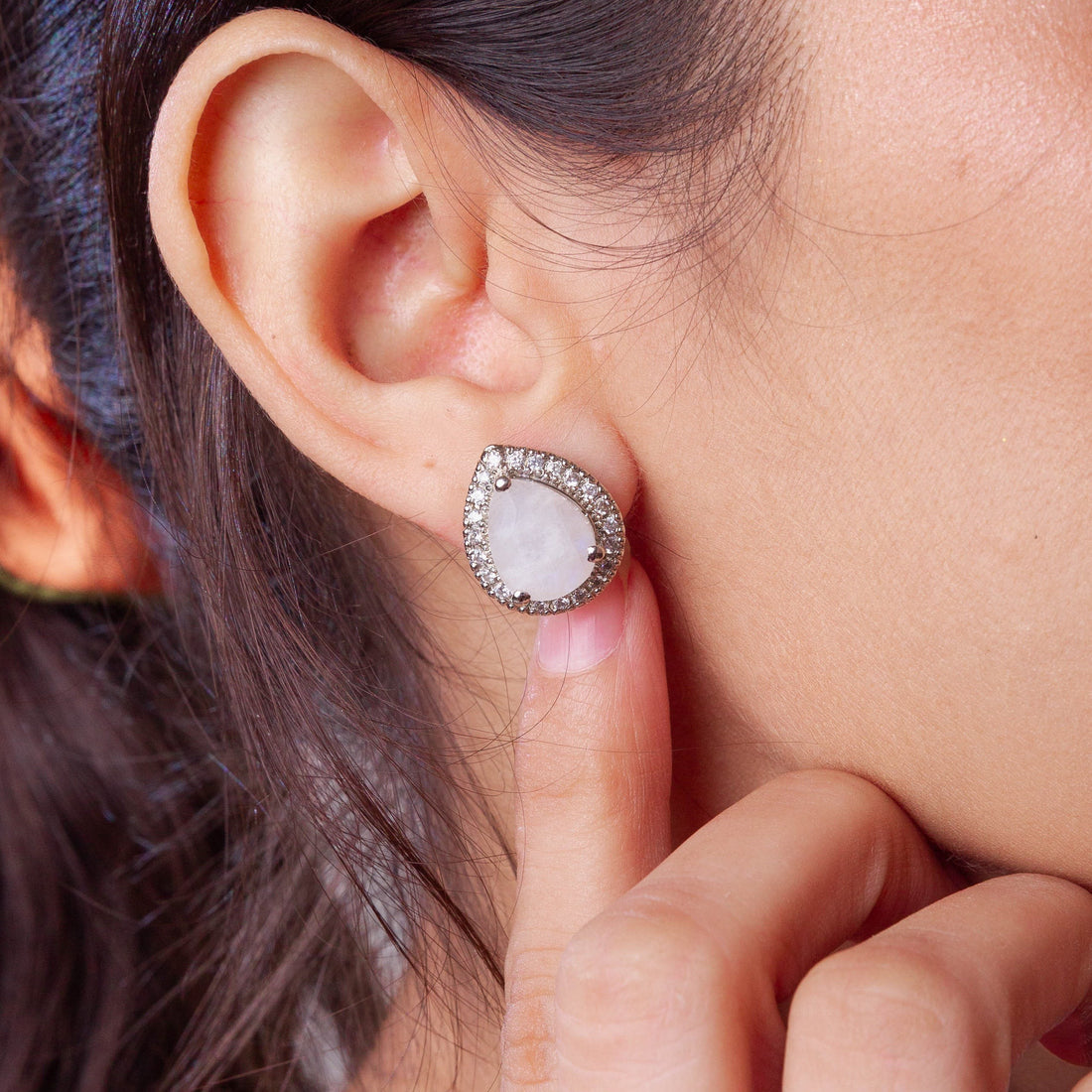 Niz & Aly moonstone earring with a teardrop shape and diamond halo setting worn on a woman's ear