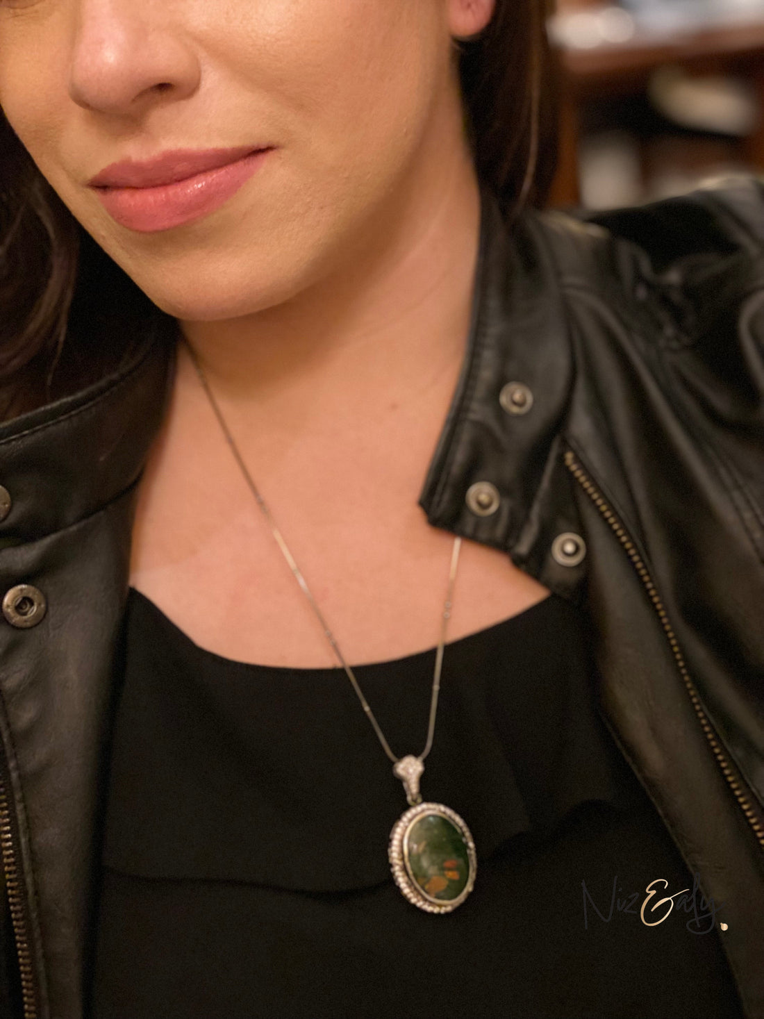 Niz & Aly natural bloodstone pendant with green and red flecks on a silver chain worn by a woman in a leather jacket