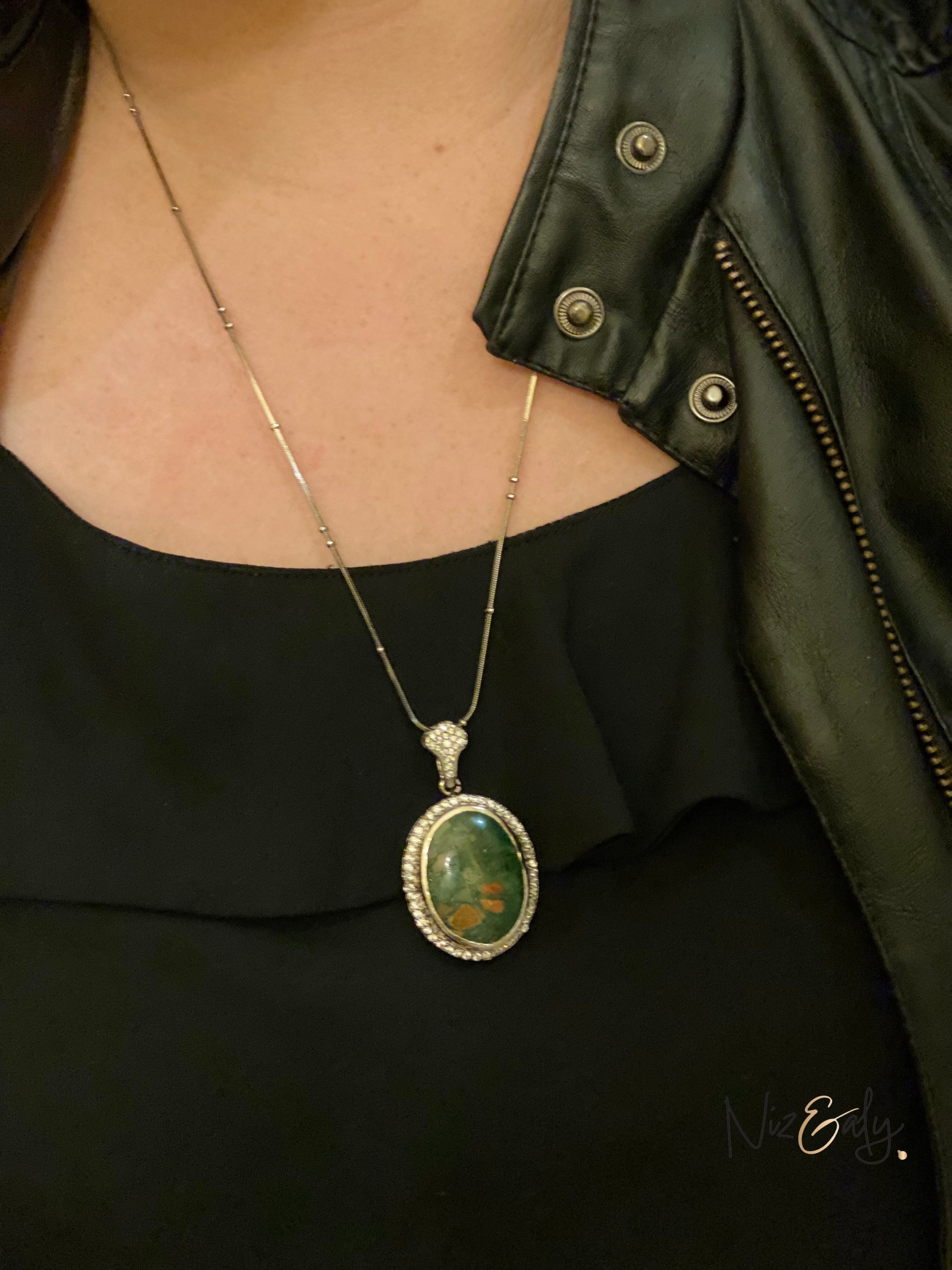 Niz & Aly oval natural bloodstone pendant with red flecks on a silver chain worn over a black top and leather jacket.