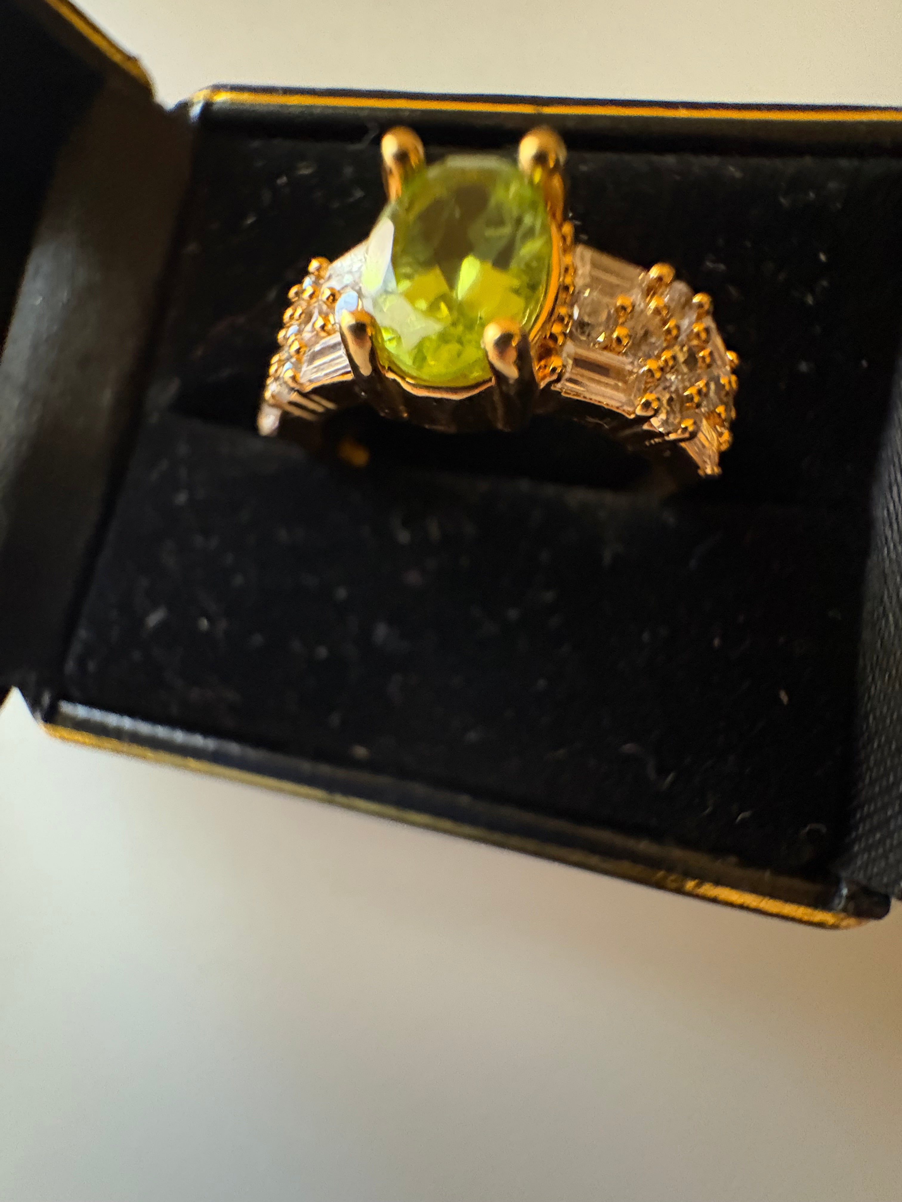 Niz & Aly natural apple green peridot ring with gold plating and sparkling cubic zirconia in a black jewelry box.