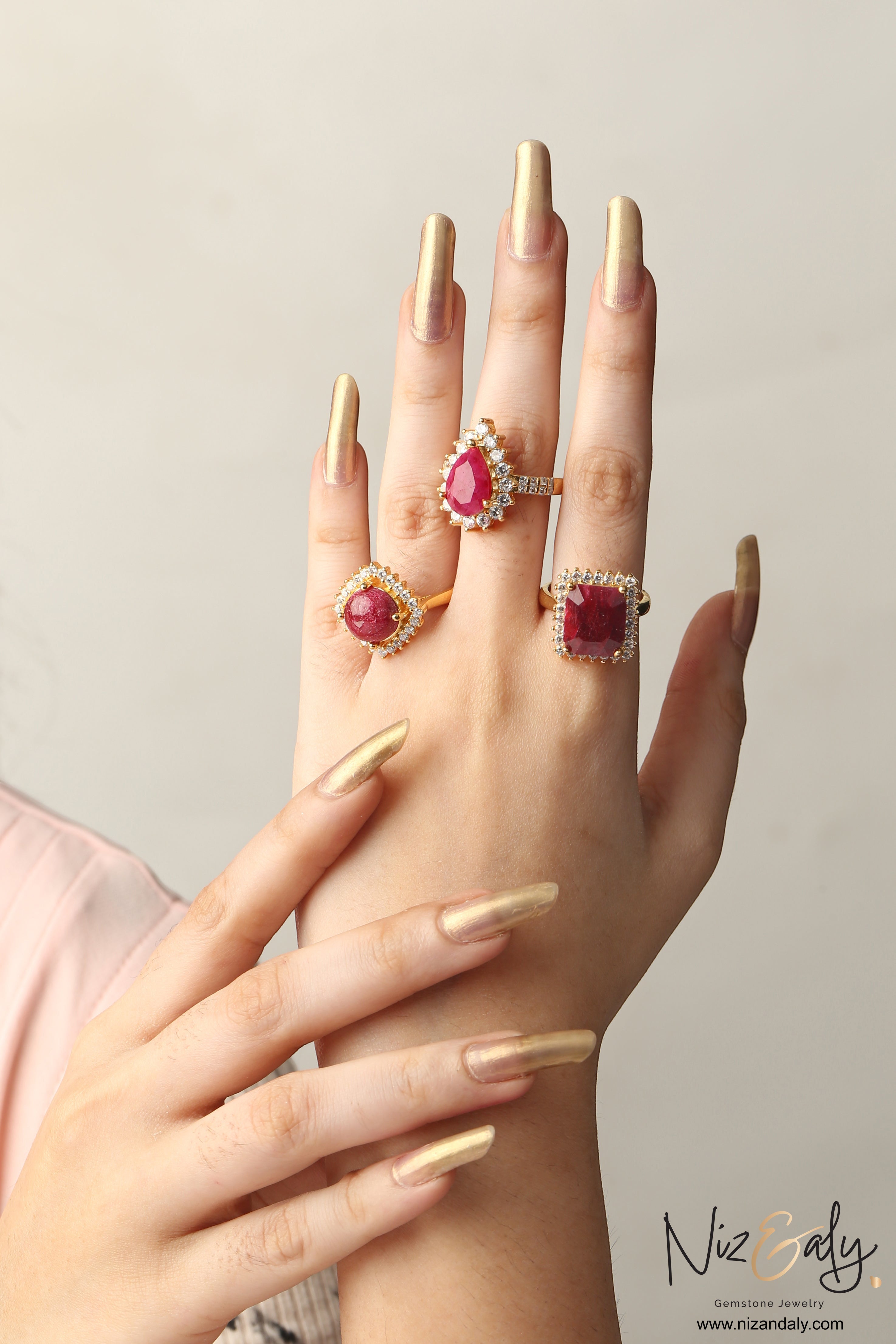 Niz & Aly natural ruby rings featuring pear, cushion, and square cuts with diamond halos on a hand with gold nails.