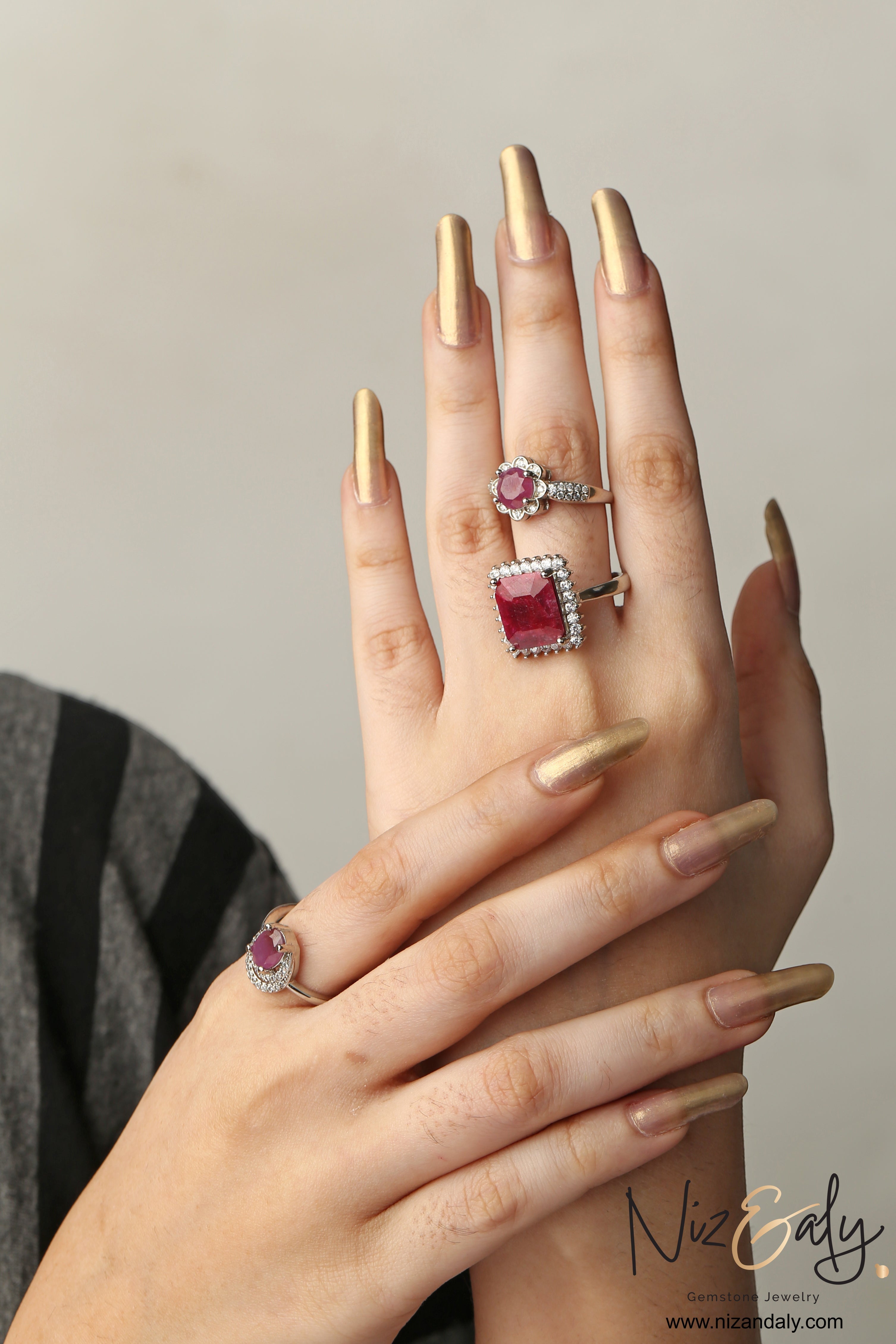 Niz & Aly natural ruby rings featuring cushion and round cut crimson gemstones set in silver bands on a model's hand.