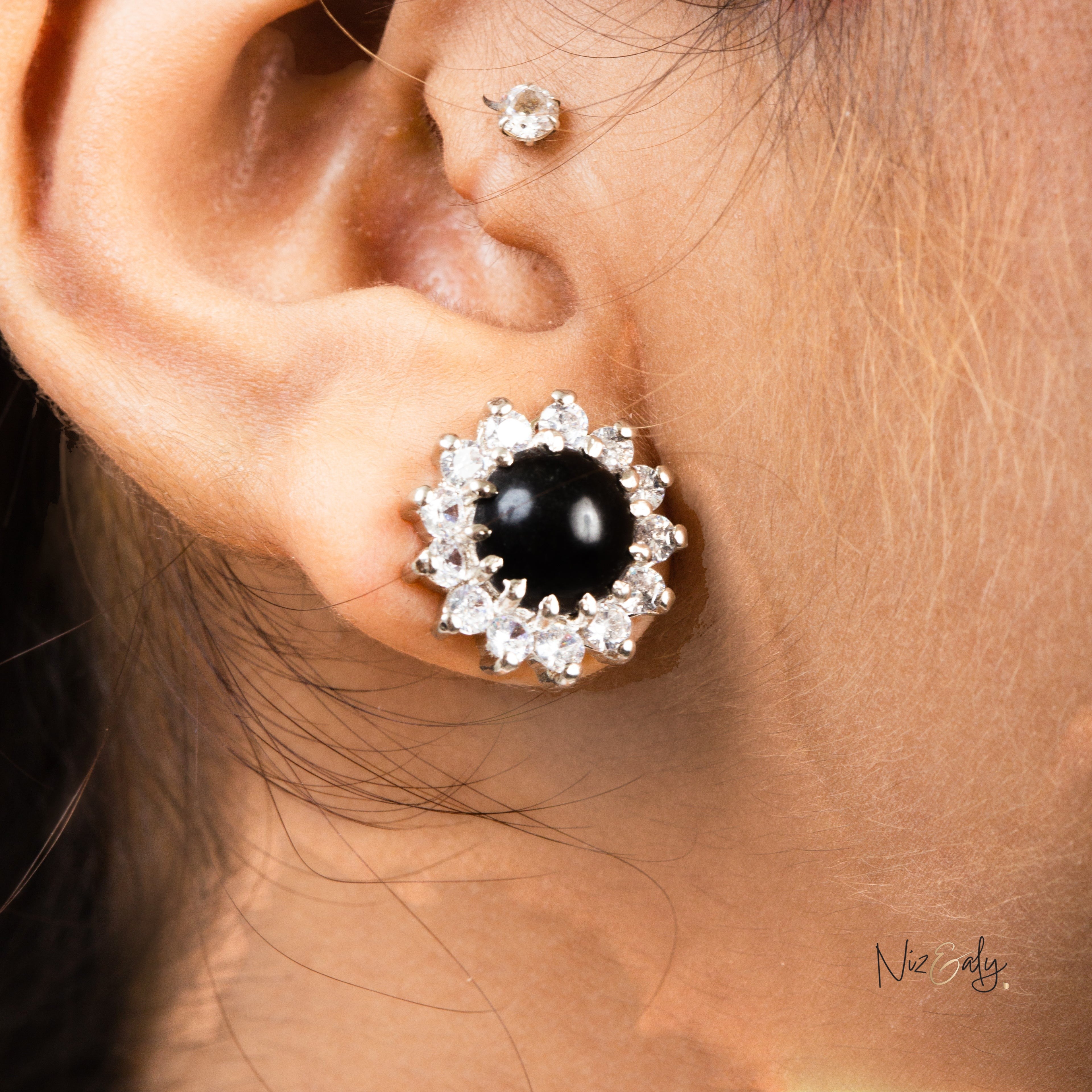 Niz & Aly black onyx cabochon stud earring surrounded by sparkling cubic zirconia worn on a pierced earlobe