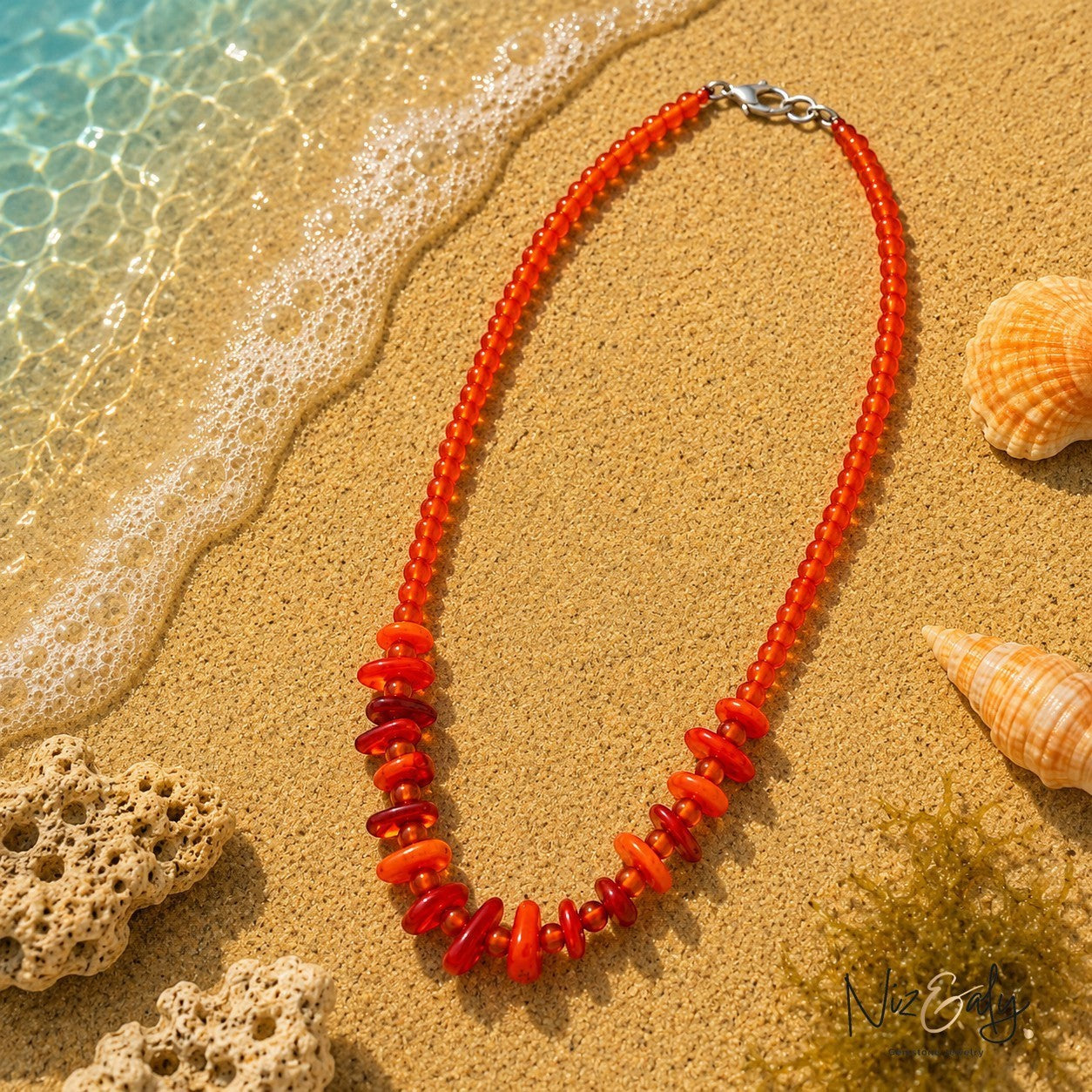 Niz & Aly orange semi-precious gemstone bead necklace with varied shapes on a sandy beach with seashells