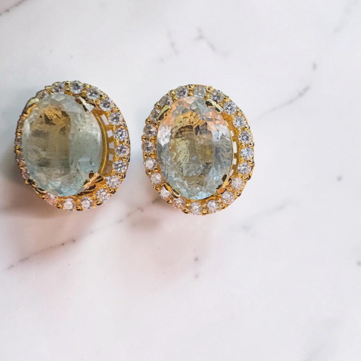 Niz & Aly oval aquamarine ear studs featuring a gold halo setting with sparkling white cubic zirconia accents.