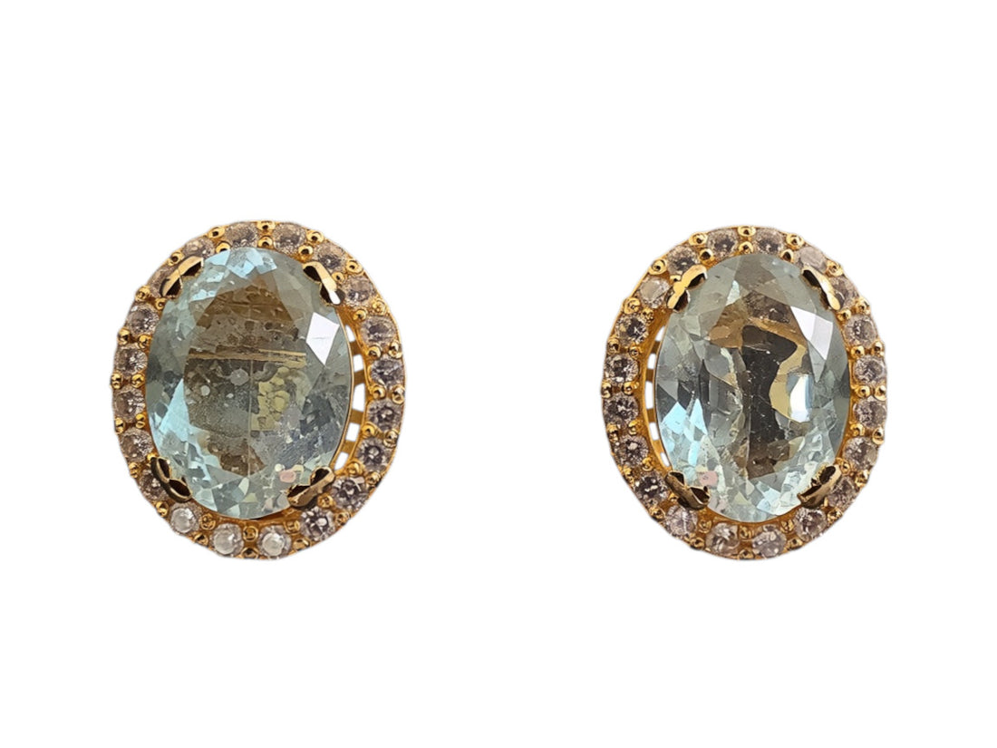 Niz & Aly oval aquamarine stud earrings featuring a gold halo setting with sparkling white accent stones.