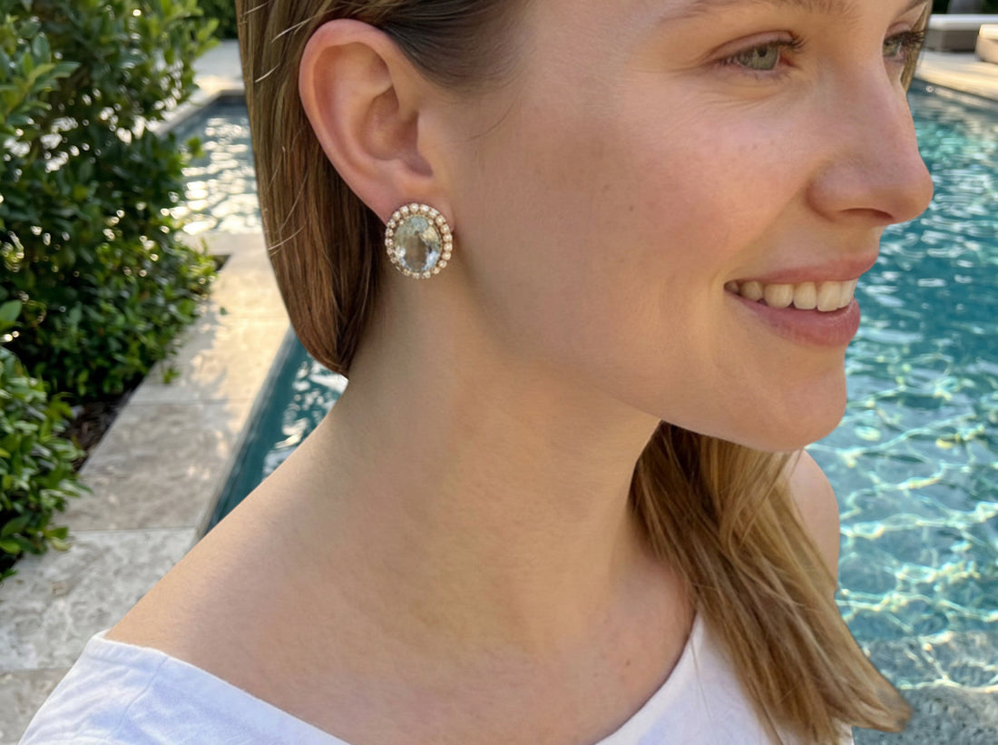 Niz & Aly oval aquamarine stud earrings with a brilliant halo setting worn by a woman near a swimming pool.