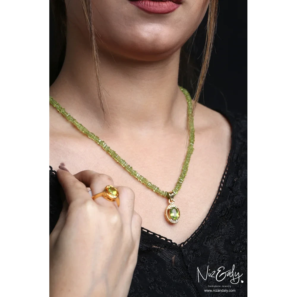 Niz & Aly oval Arizona peridot pendant necklace and gold-plated ring worn by a woman against a black background.