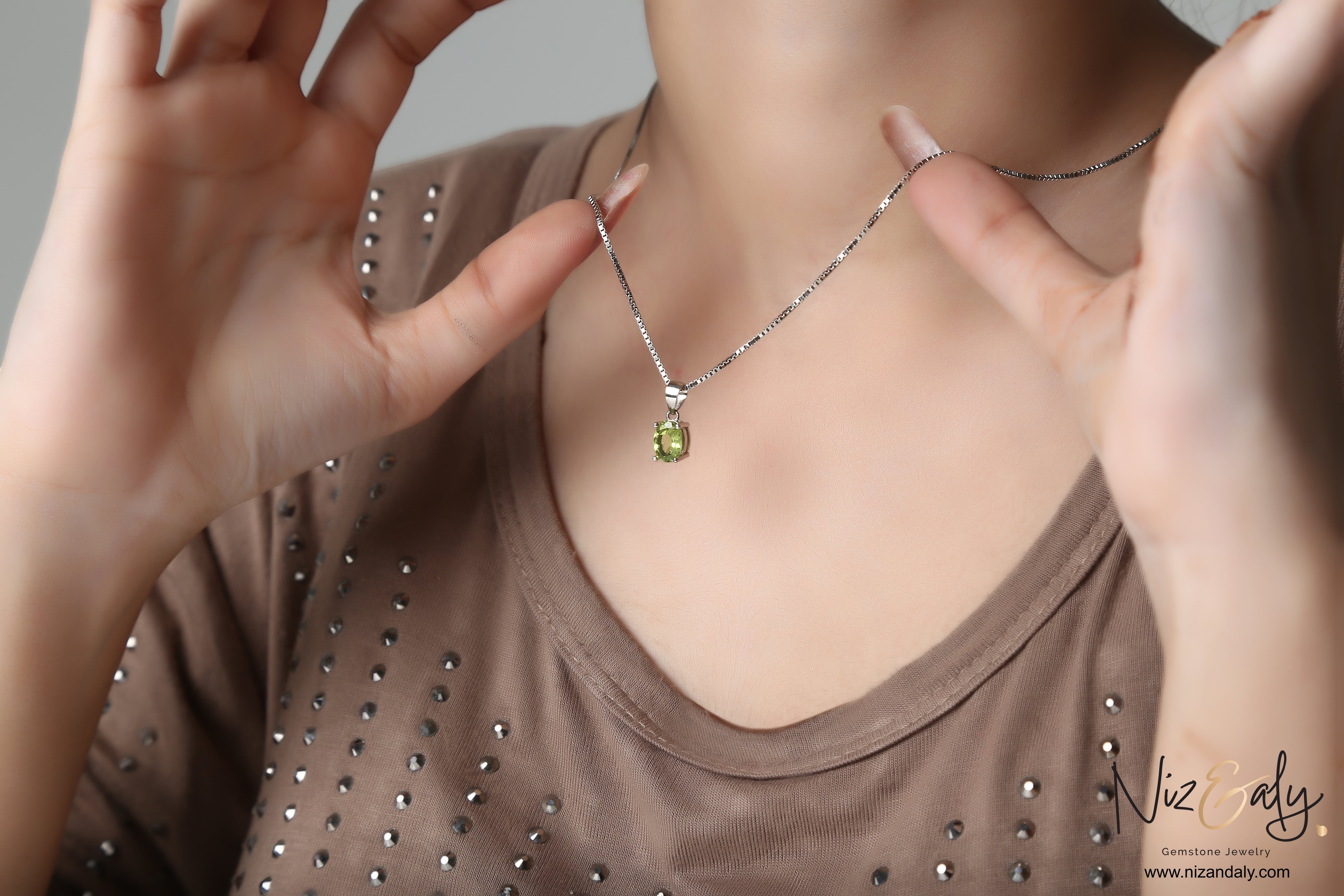 Niz & Aly oval-cut peridot solitaire pendant on a silver chain worn by a woman in a brown embellished top