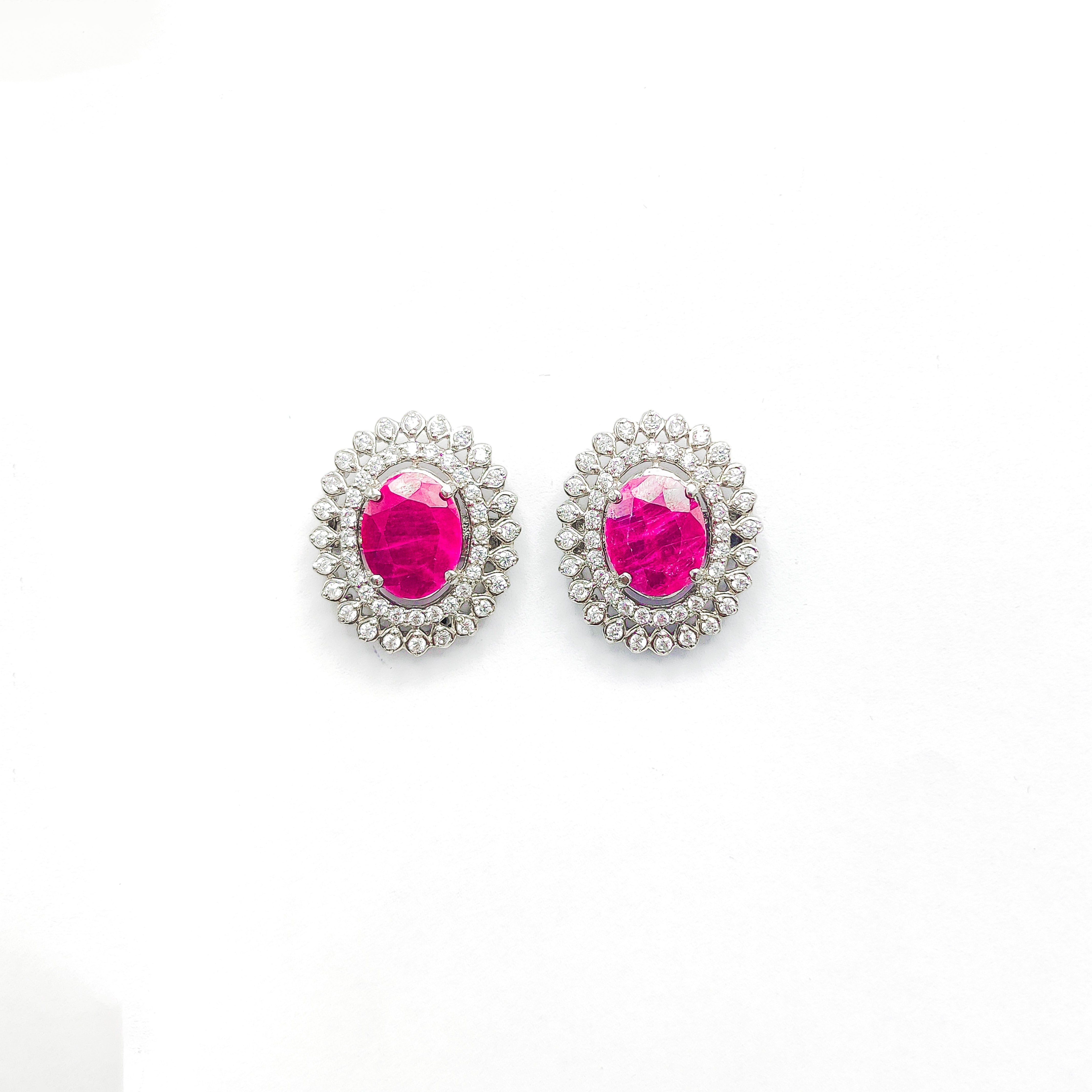 Niz & Aly oval African ruby stud earrings surrounded by a halo of sparkling white diamonds on a white background.
