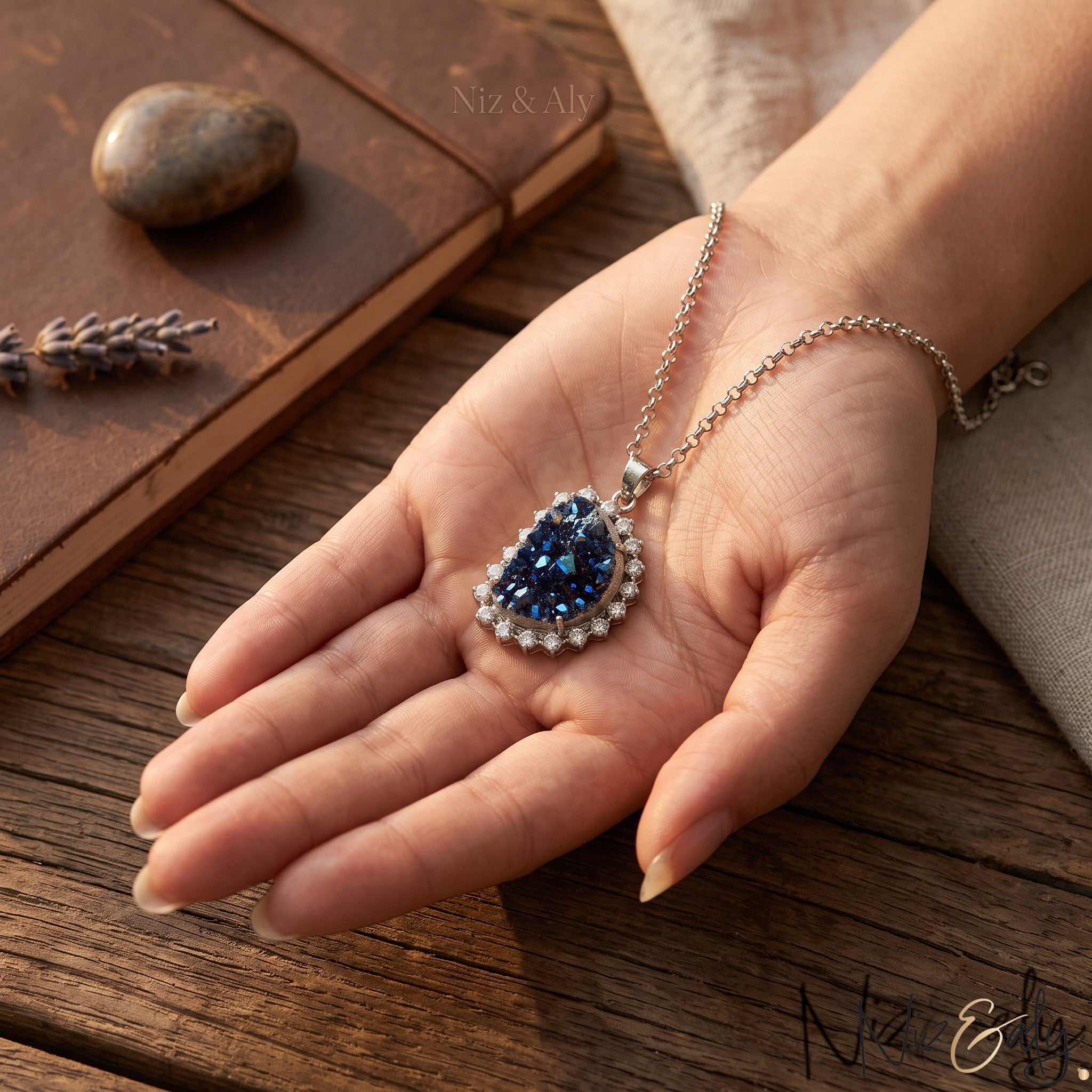 Niz & Aly peacock ore bornite pendant featuring iridescent blue crystals set in a sterling silver chain on a hand.