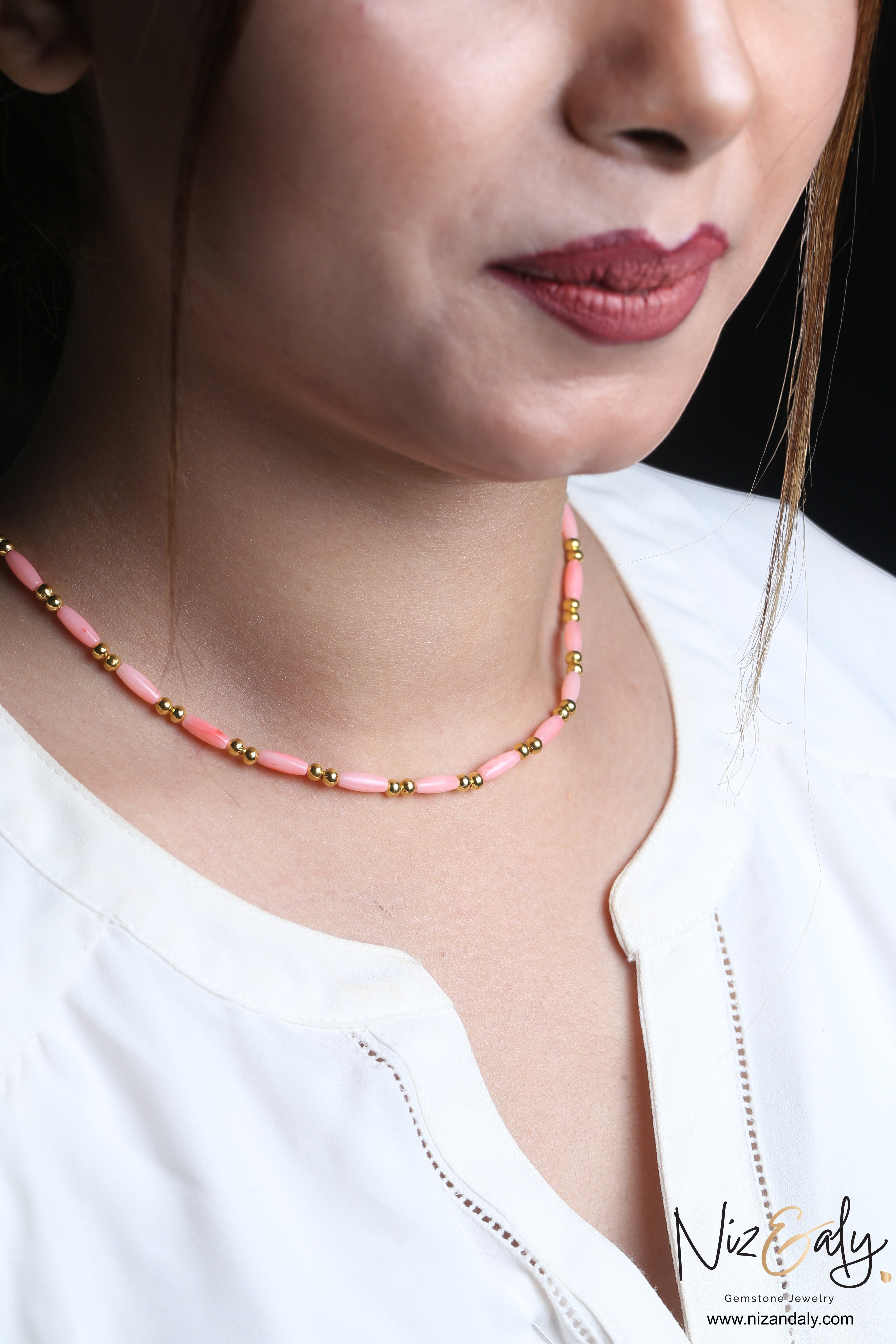 Niz & Aly dainty pink rice-shaped coral necklace with small gold beads worn by a woman in a white top