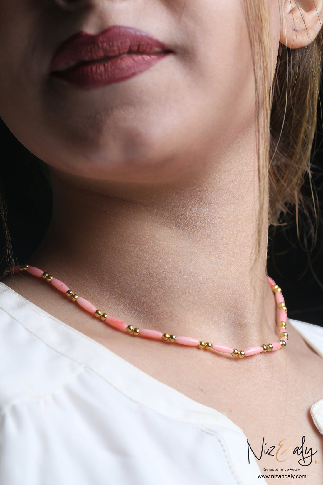 Niz & Aly dainty pink rice-shaped coral necklace with small gold beads worn by a woman against a black background