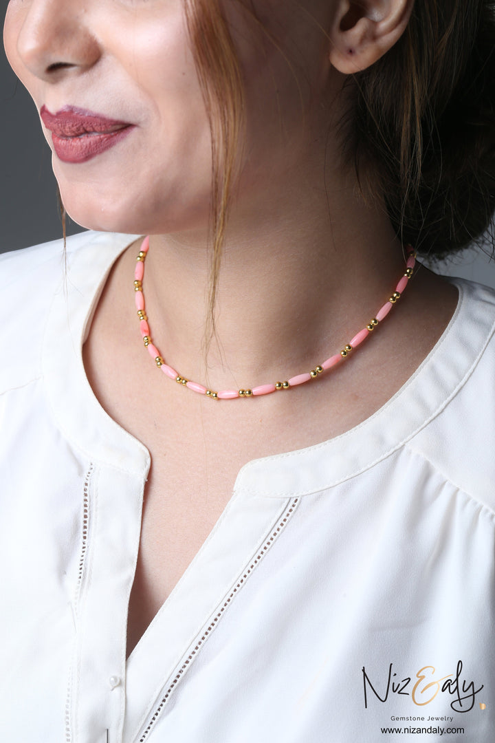 Niz & Aly dainty pink rice-shaped coral necklace with gold beads worn by a woman in a white blouse