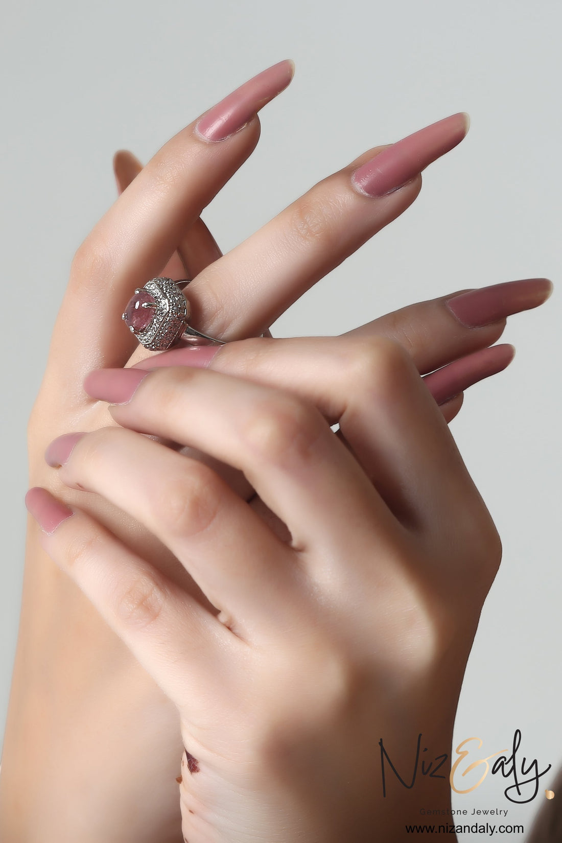 Niz & Aly square pink tourmaline ring with diamond halo setting worn on a hand with matching pink manicured nails