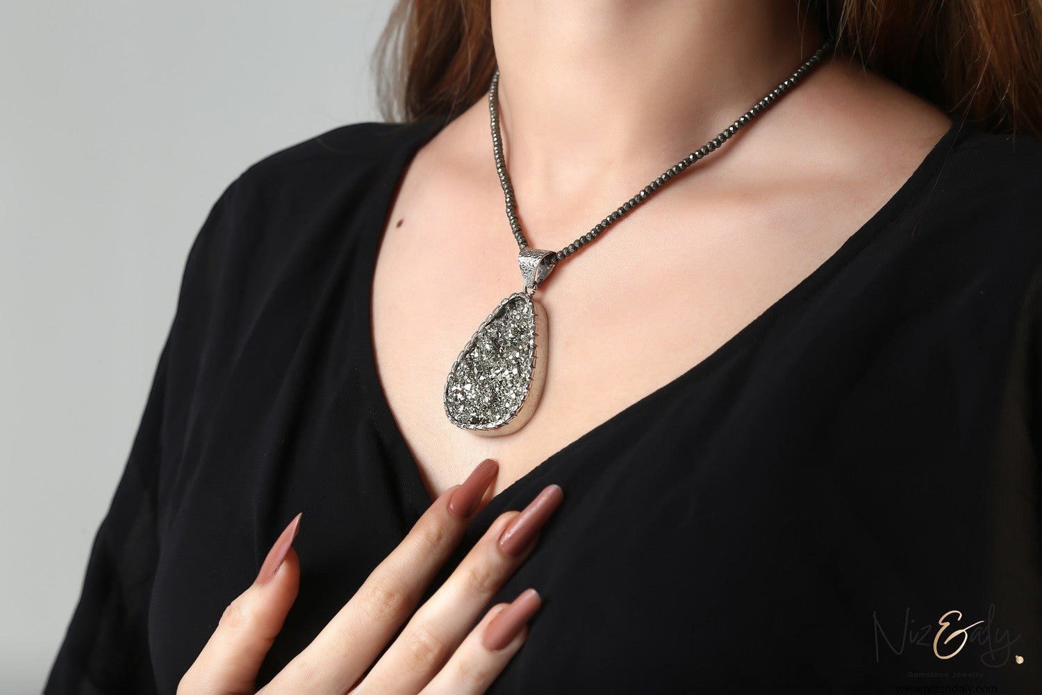 Niz & Aly oval natural pyrite pendant on a strand of faceted pyrite beads worn by a woman in a black top