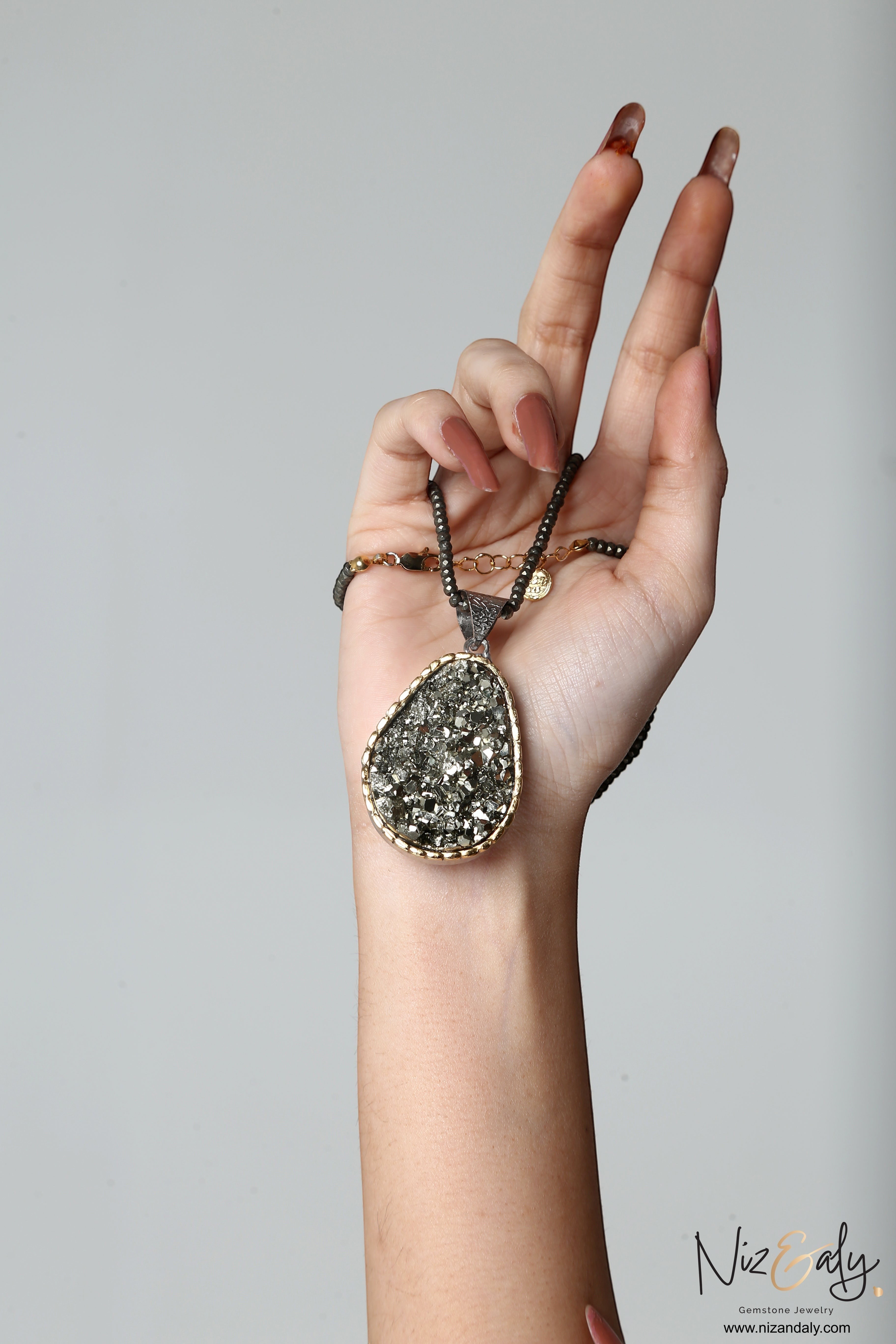 Niz & Aly natural pyrite pendant necklace with faceted pyrite beads and sterling silver setting held in a hand