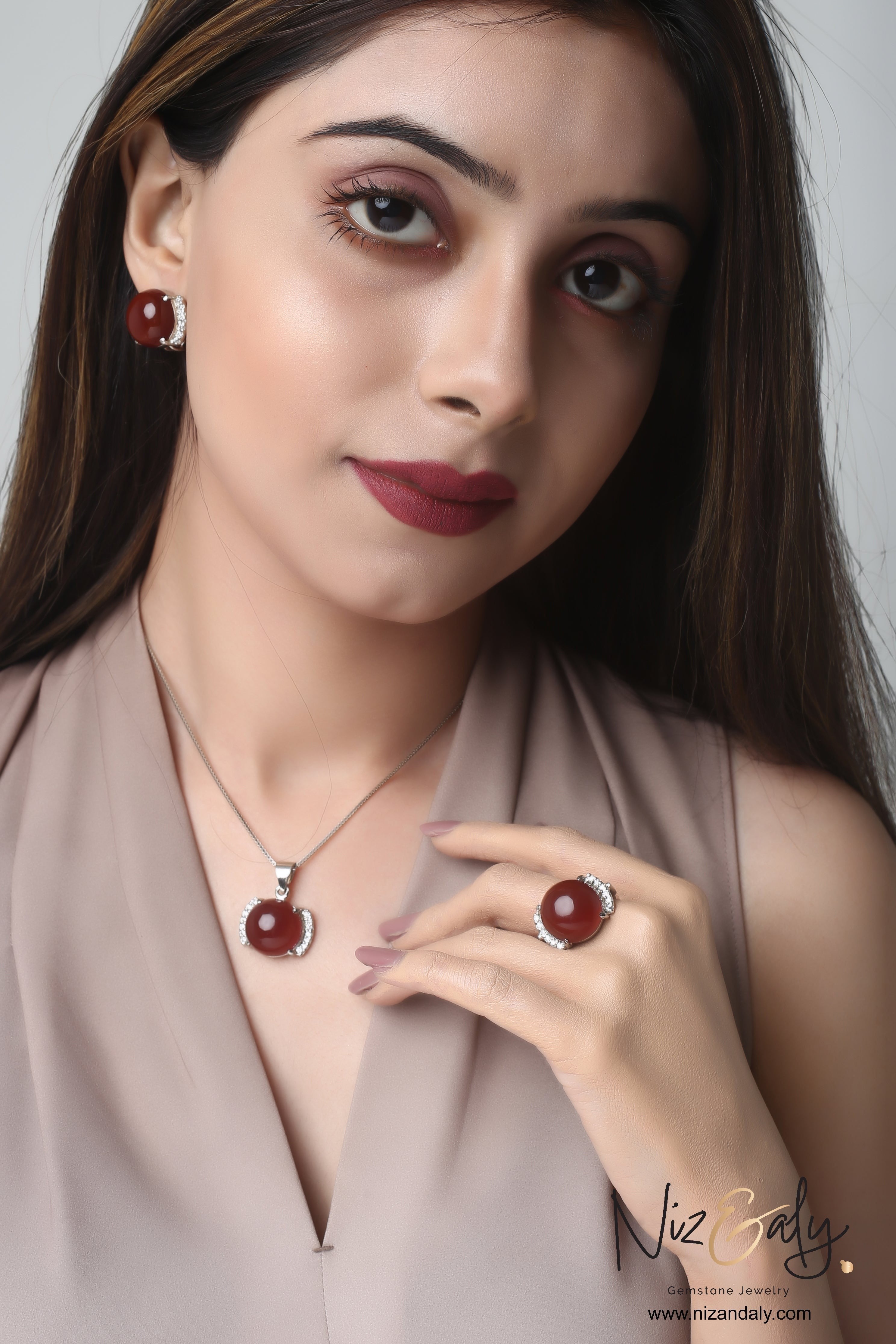 Niz & Aly red agate pendant set with matching earrings and ring worn by a woman in a beige top.