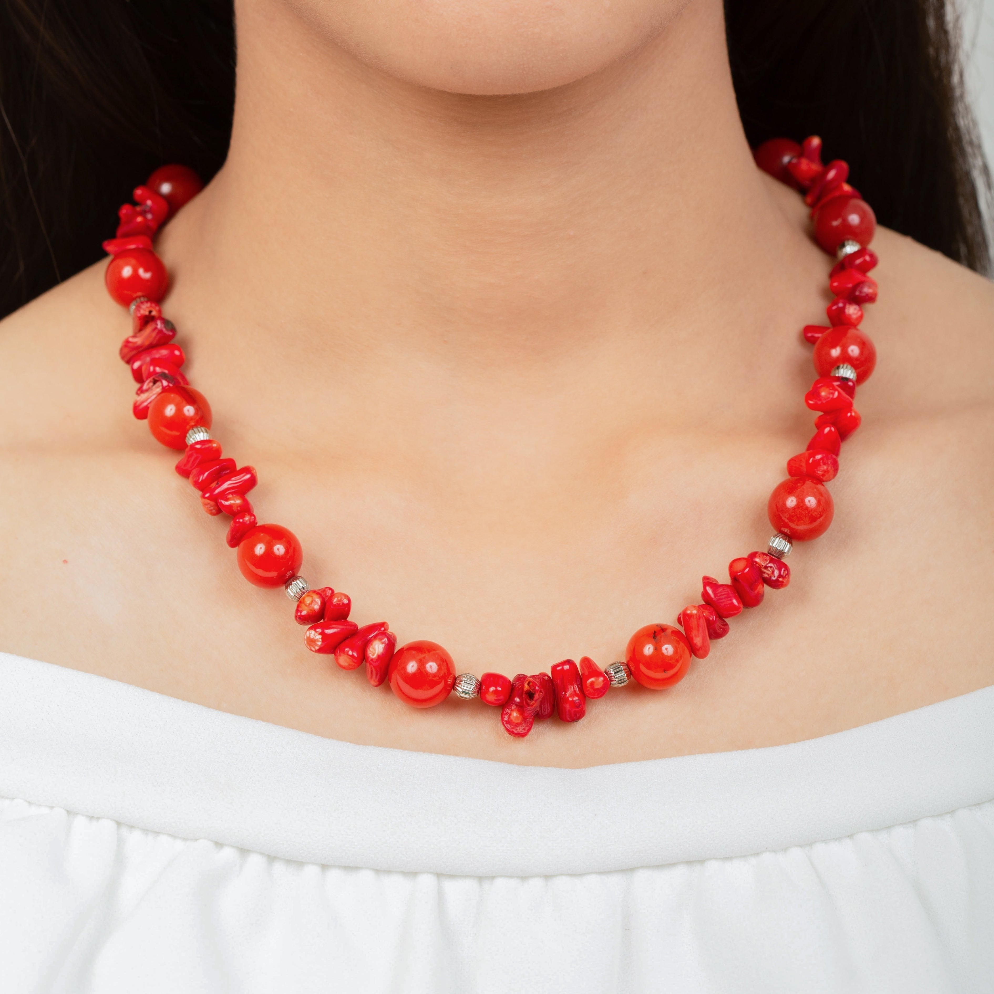 Niz & Aly necklace featuring vibrant red natural coral and polished carnelian beads worn by a woman in a white top.
