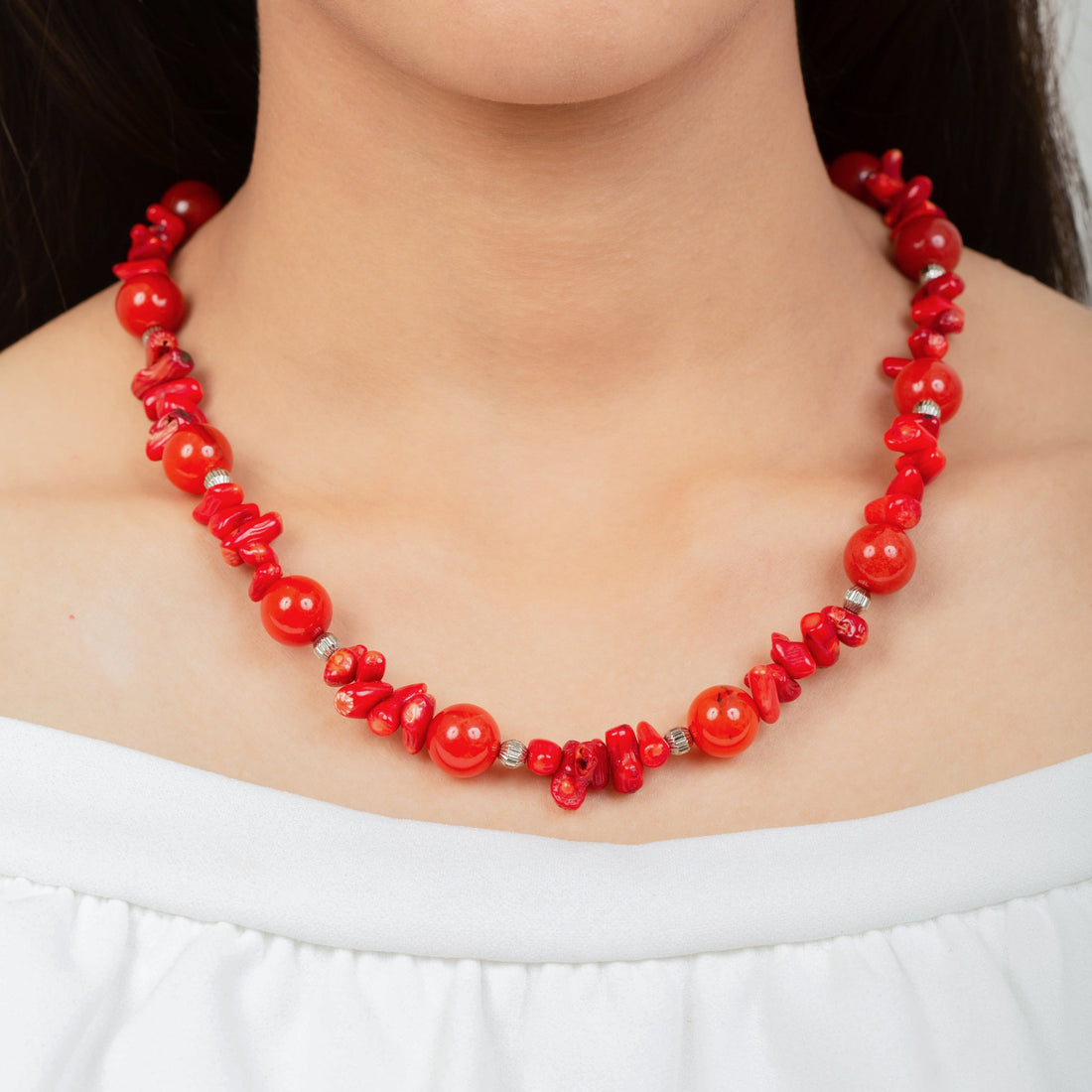 Niz & Aly necklace featuring vibrant red natural coral and polished carnelian beads worn by a woman in a white top.