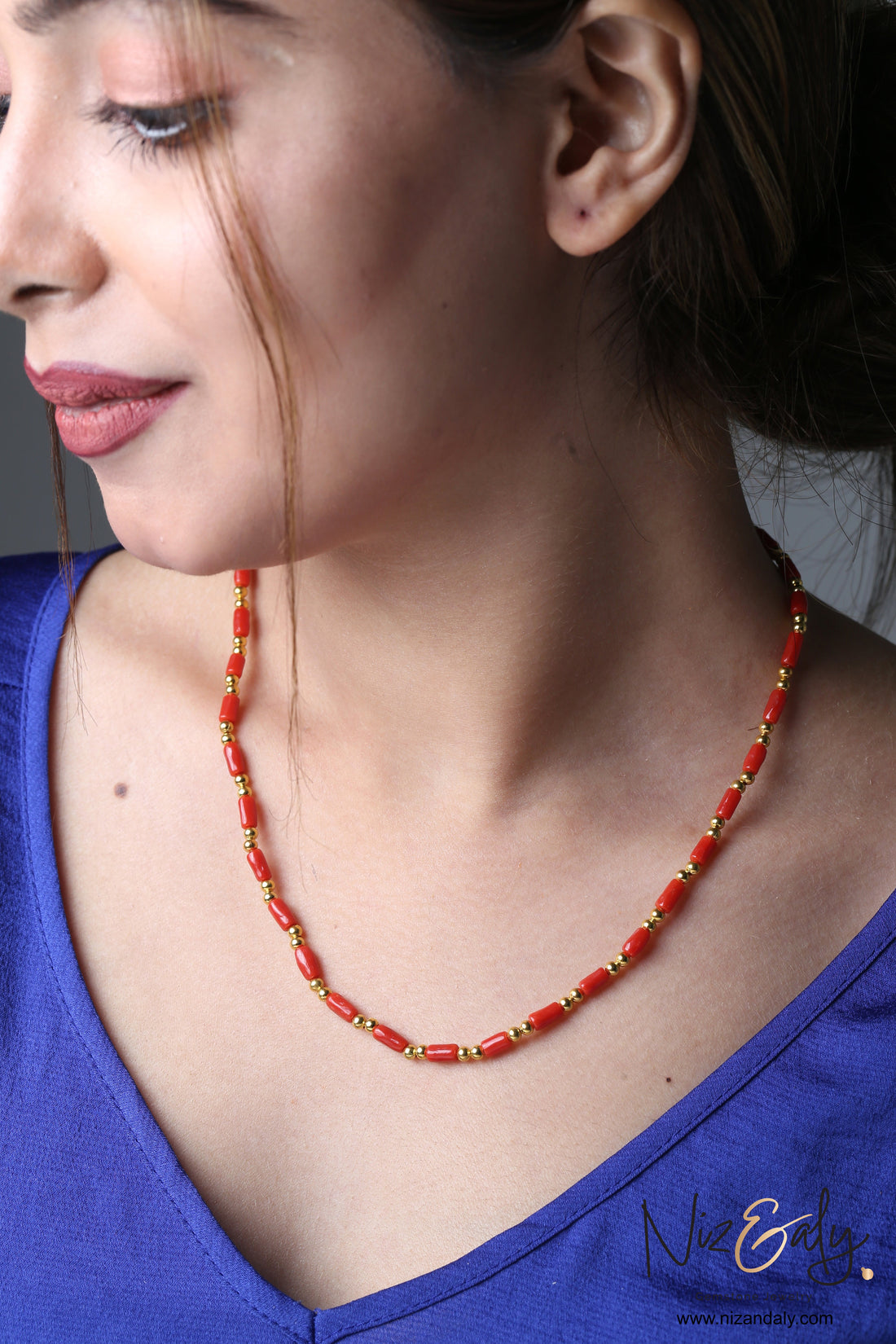Niz & Aly natural red coral barrel bead necklace with gold accents worn by a woman in a blue top