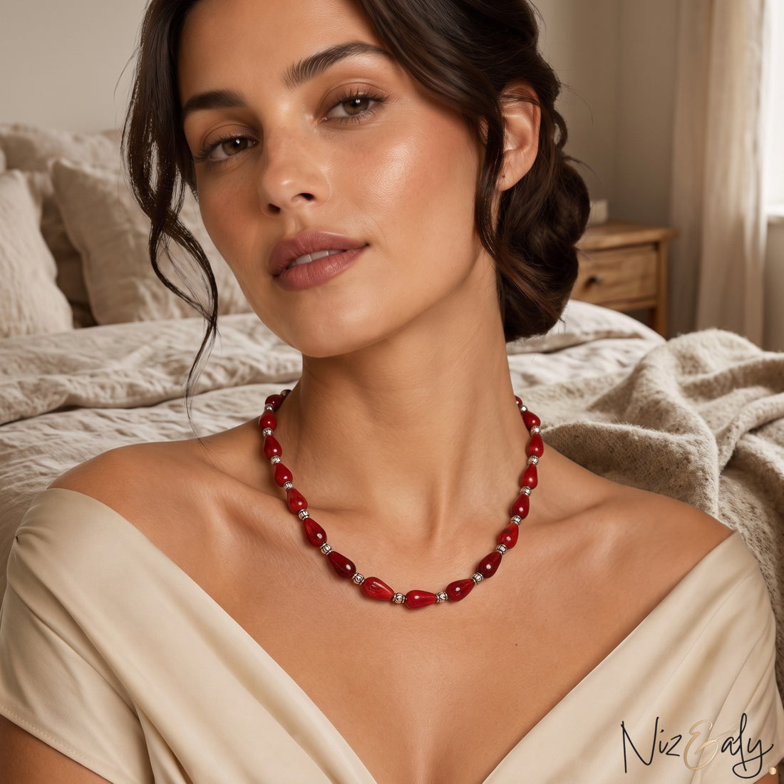 Niz & Aly Rossa Lacrima necklace featuring natural red coral teardrop beads on a woman wearing a beige off-shoulder top.