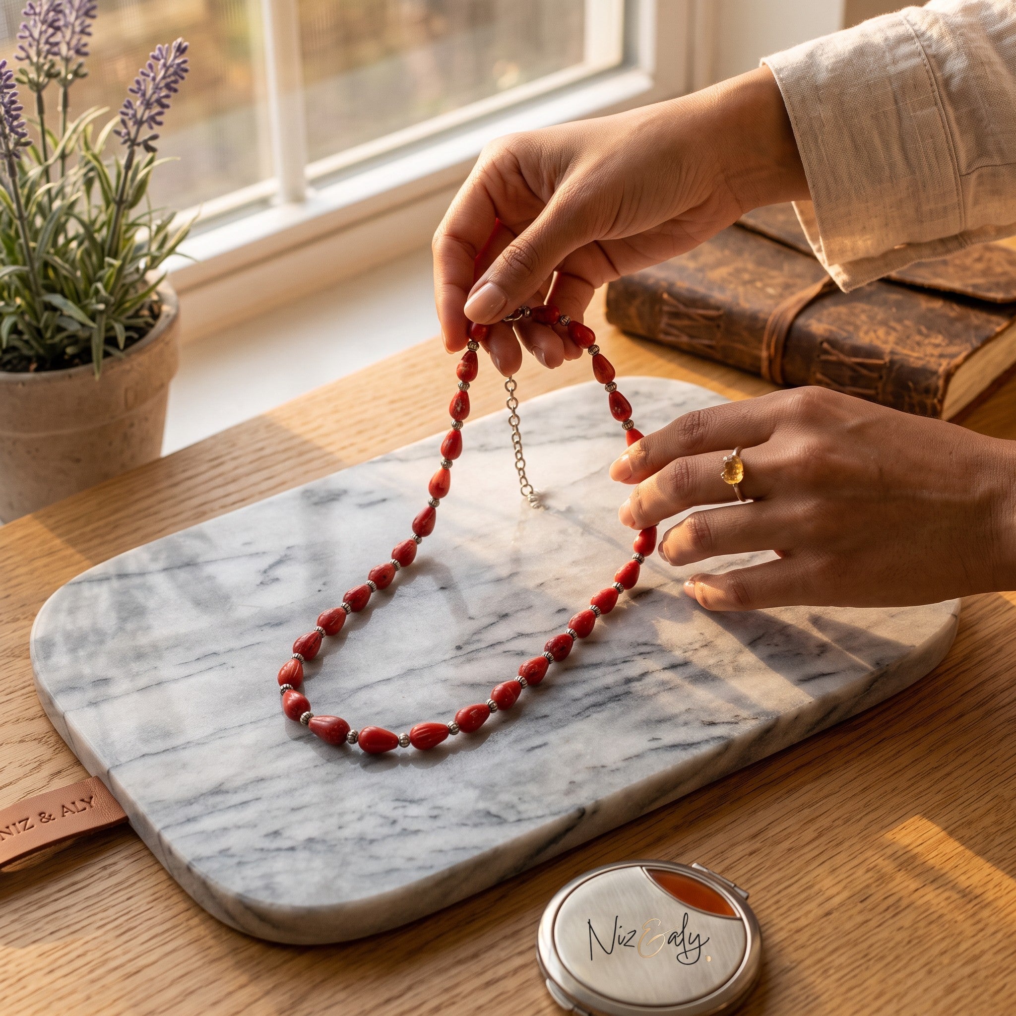 Niz & Aly Rossa Lacrima necklace featuring natural red coral teardrop beads on a marble board by a window.