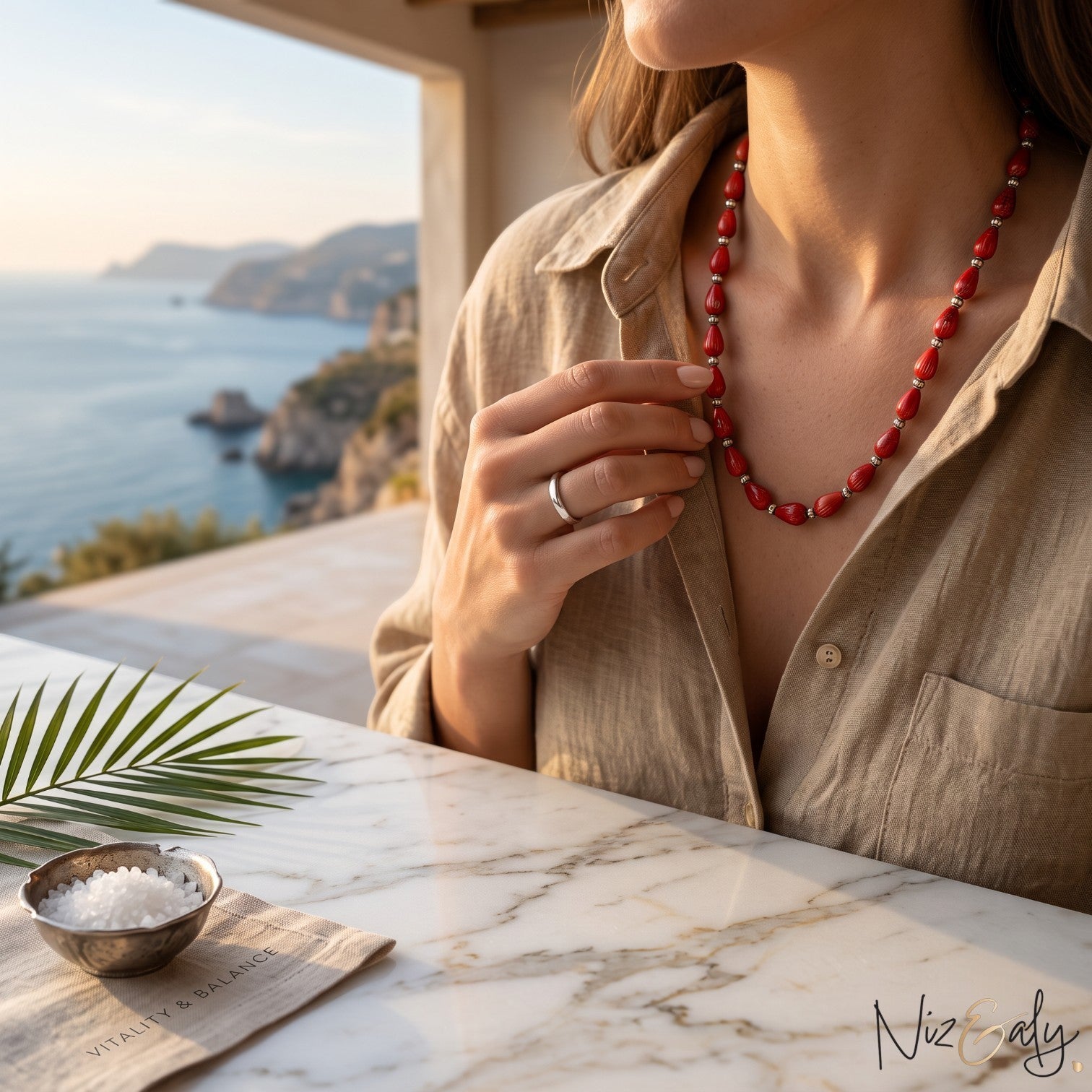 Niz & Aly Rosso Lacrima necklace featuring natural red coral teardrop beads on a woman overlooking the Mediterranean.