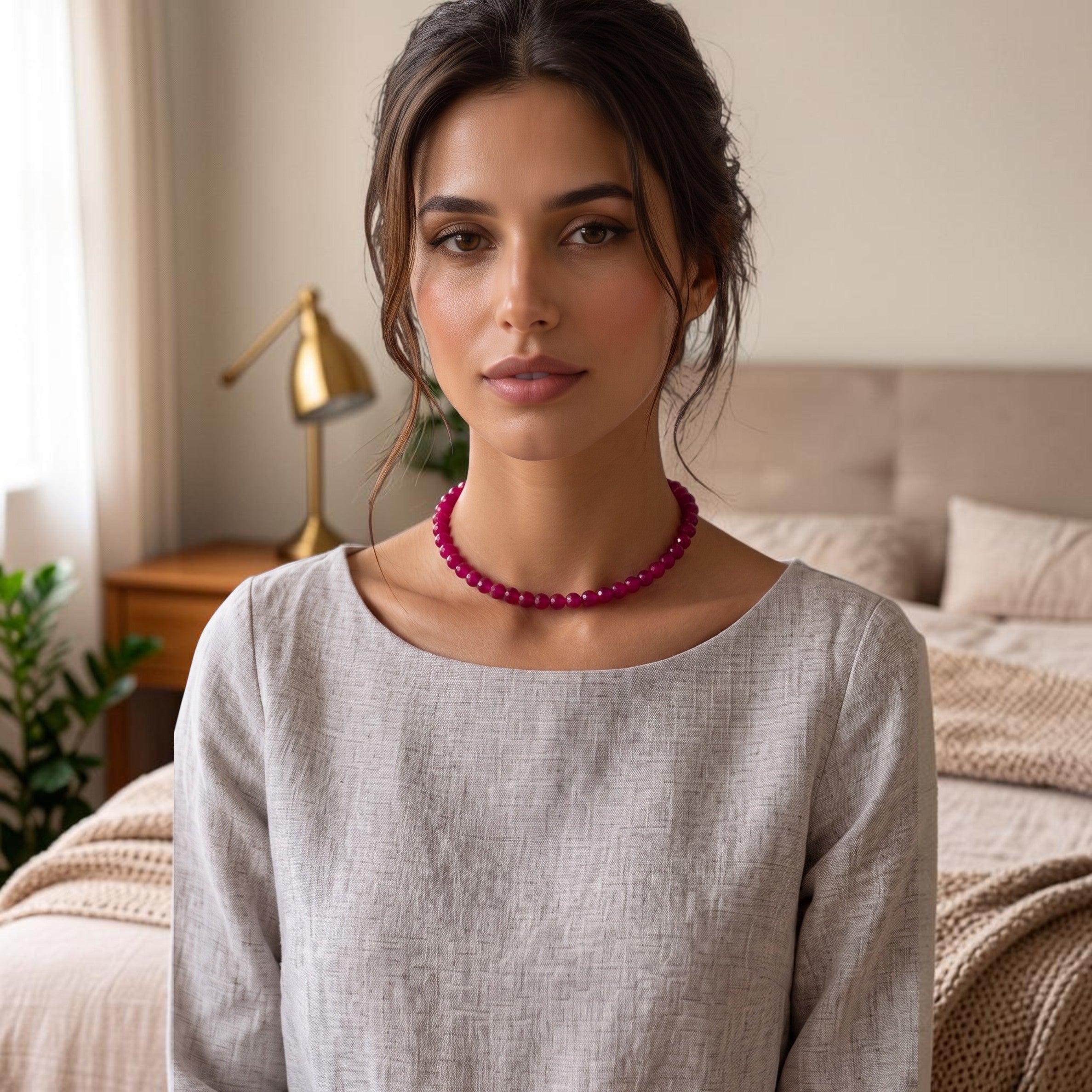 Niz & Aly red jade bead strand necklace worn by a woman in a grey linen top in a soft bedroom setting