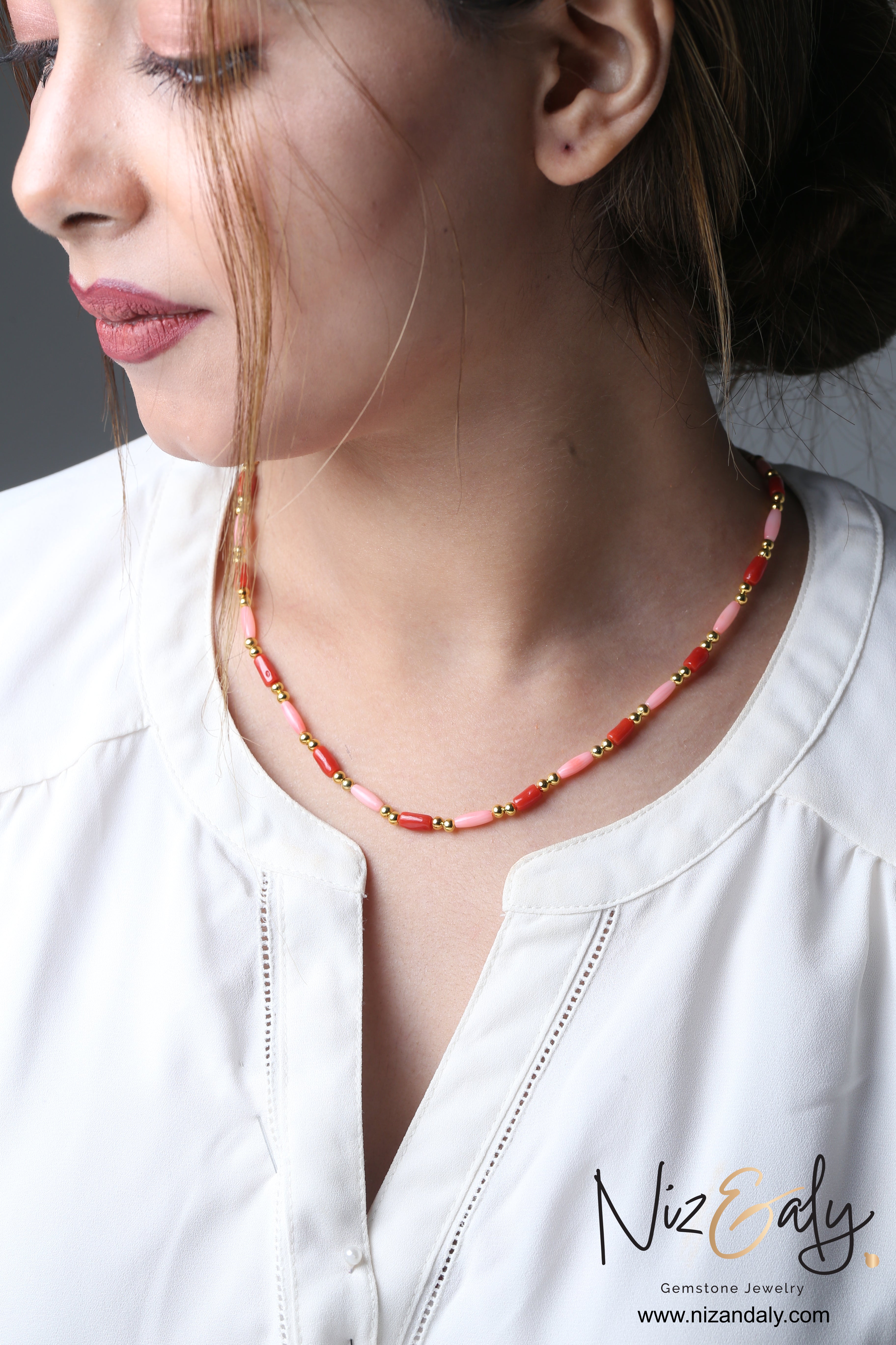 Niz & Aly dainty necklace featuring red and pink rice-shaped coral beads with gold accents worn by a woman