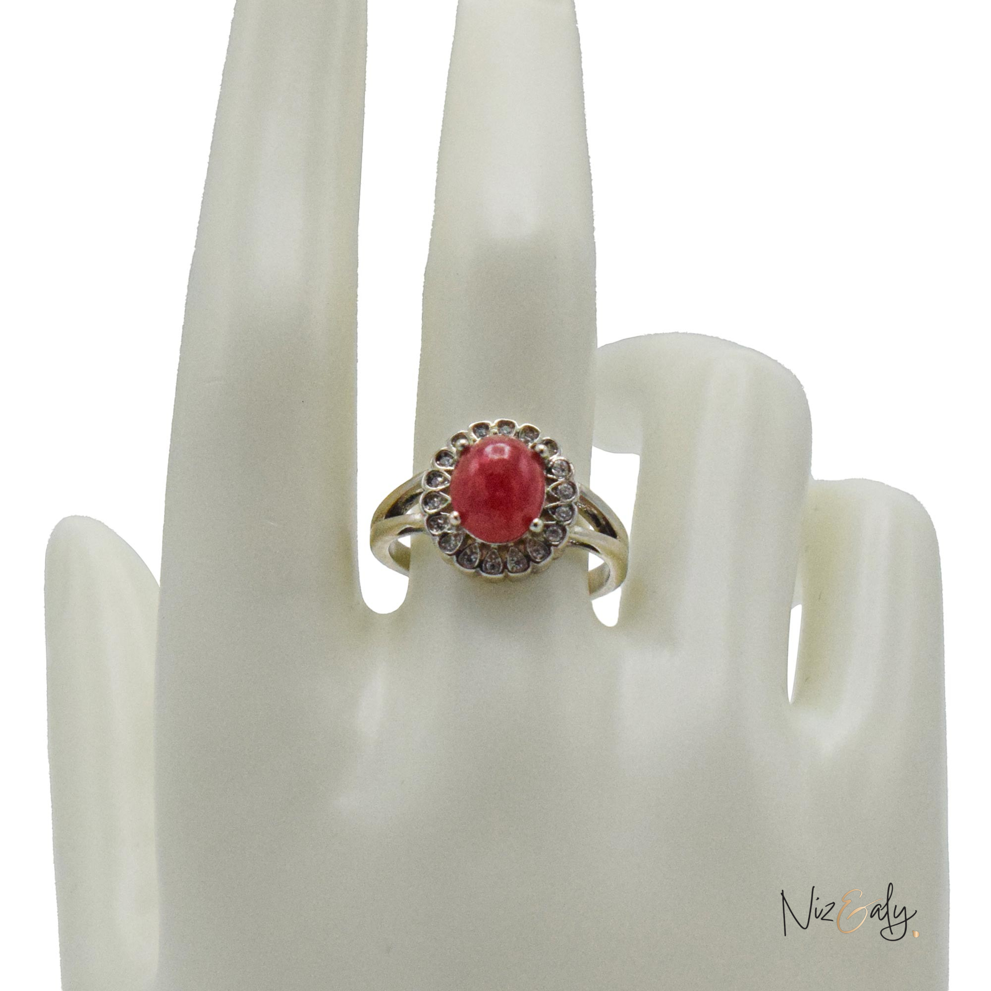 Niz & Aly red cabochon rubelite tourmaline ring with a halo of sparkling stones on a white display hand