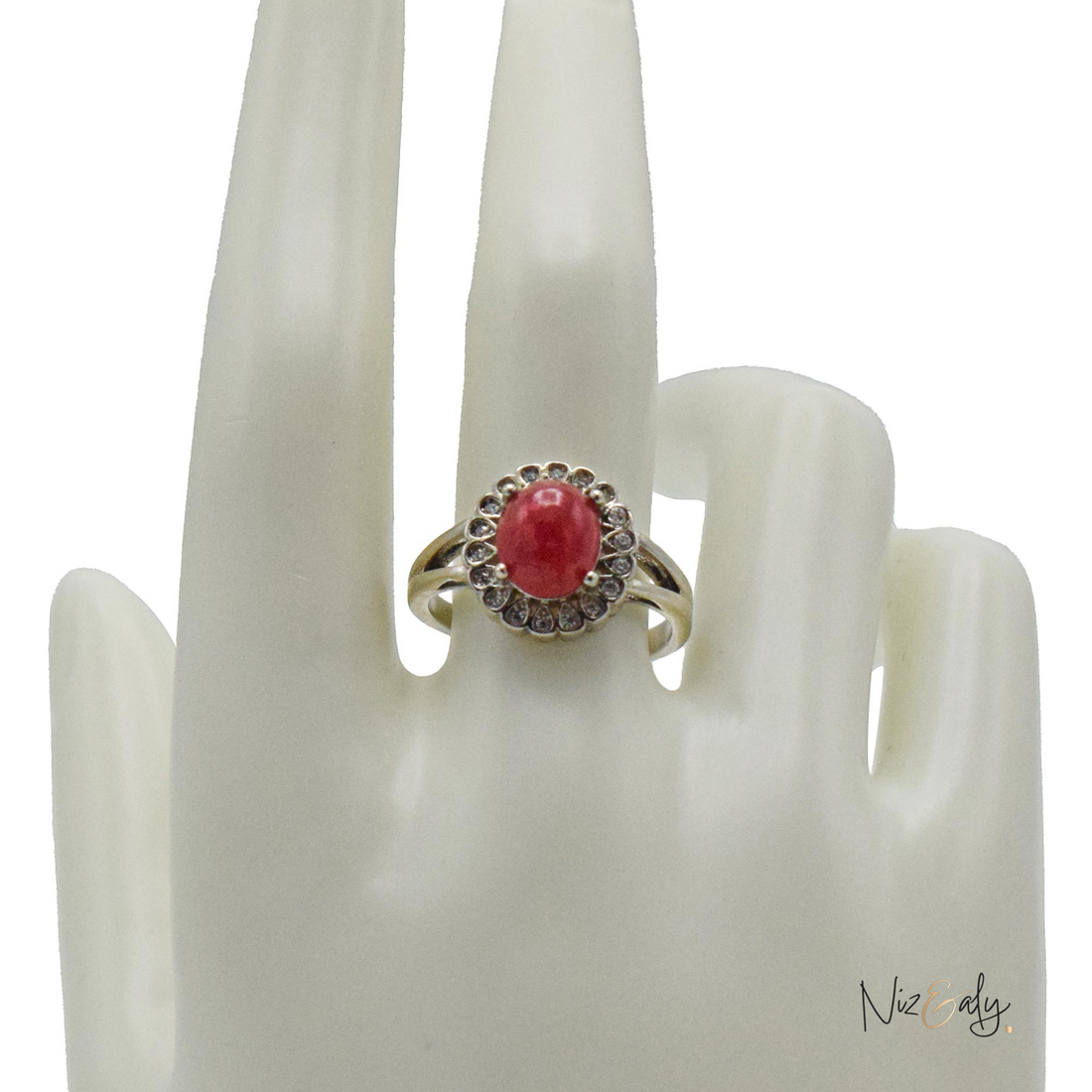 Niz & Aly red cabochon rubelite tourmaline ring with a halo of sparkling stones on a white display hand