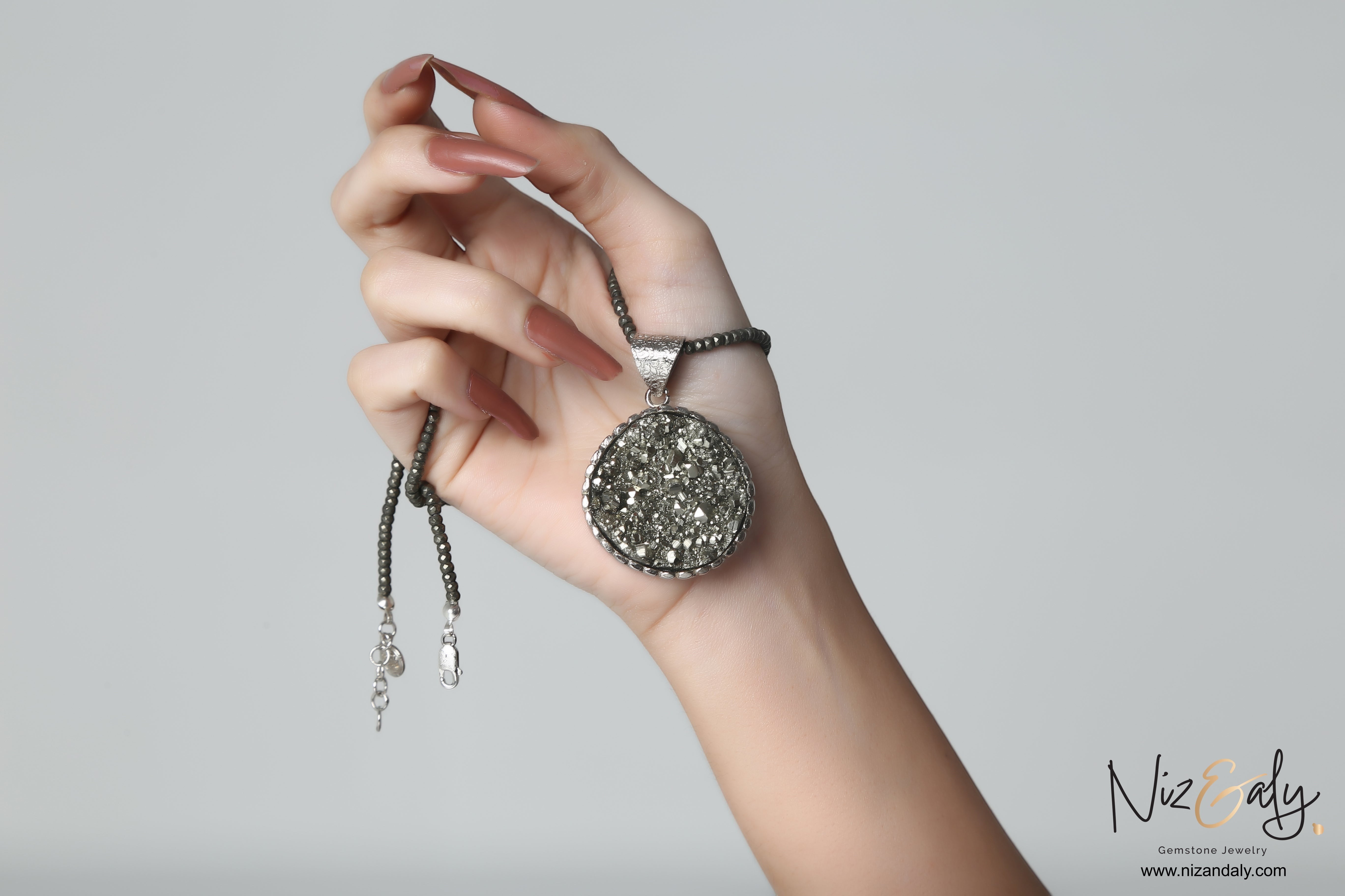Niz & Aly round pyrite pendant on a faceted pyrite bead necklace with metallic gold luster held in a hand.