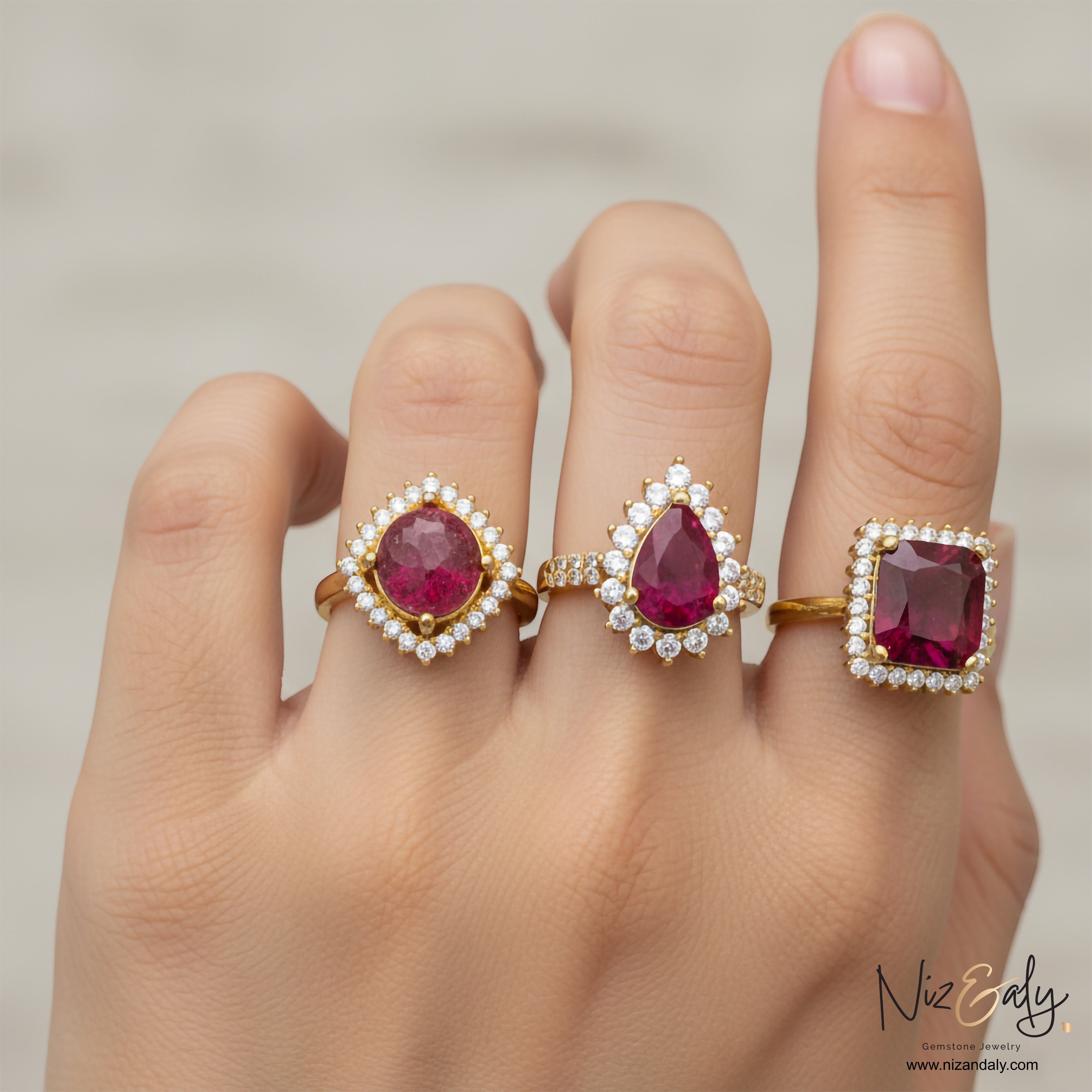 Niz & Aly ruby rings featuring oval, pear, and cushion cut natural rubies with diamond halos on gold bands on a hand.