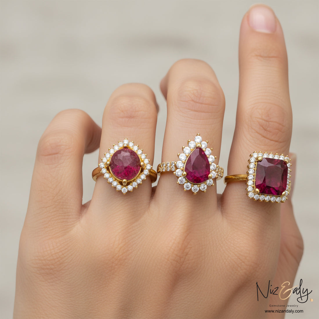 Niz & Aly ruby rings featuring oval, pear, and cushion cut natural rubies with diamond halos on gold bands on a hand.