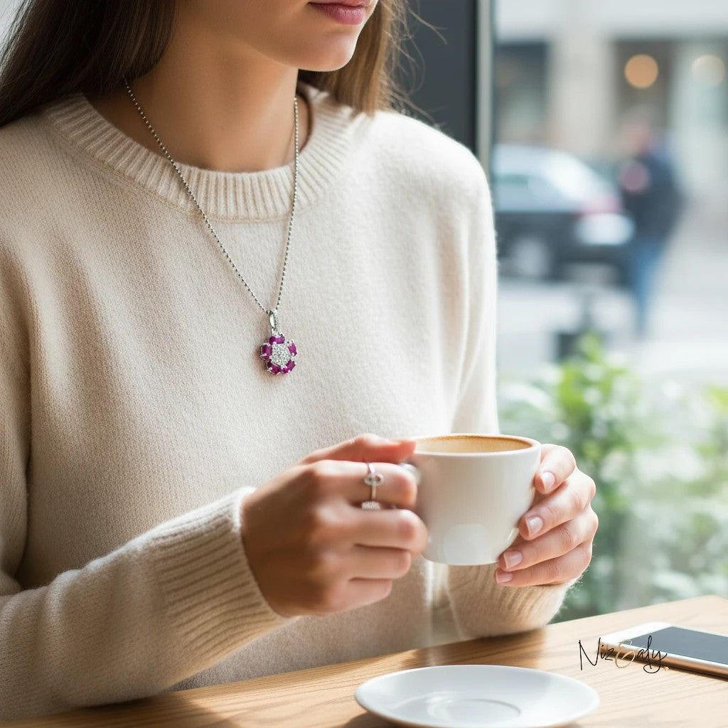 Niz & Aly red ruby flower pendant with intricate silver center worn by a woman in a cream sweater holding a coffee cup