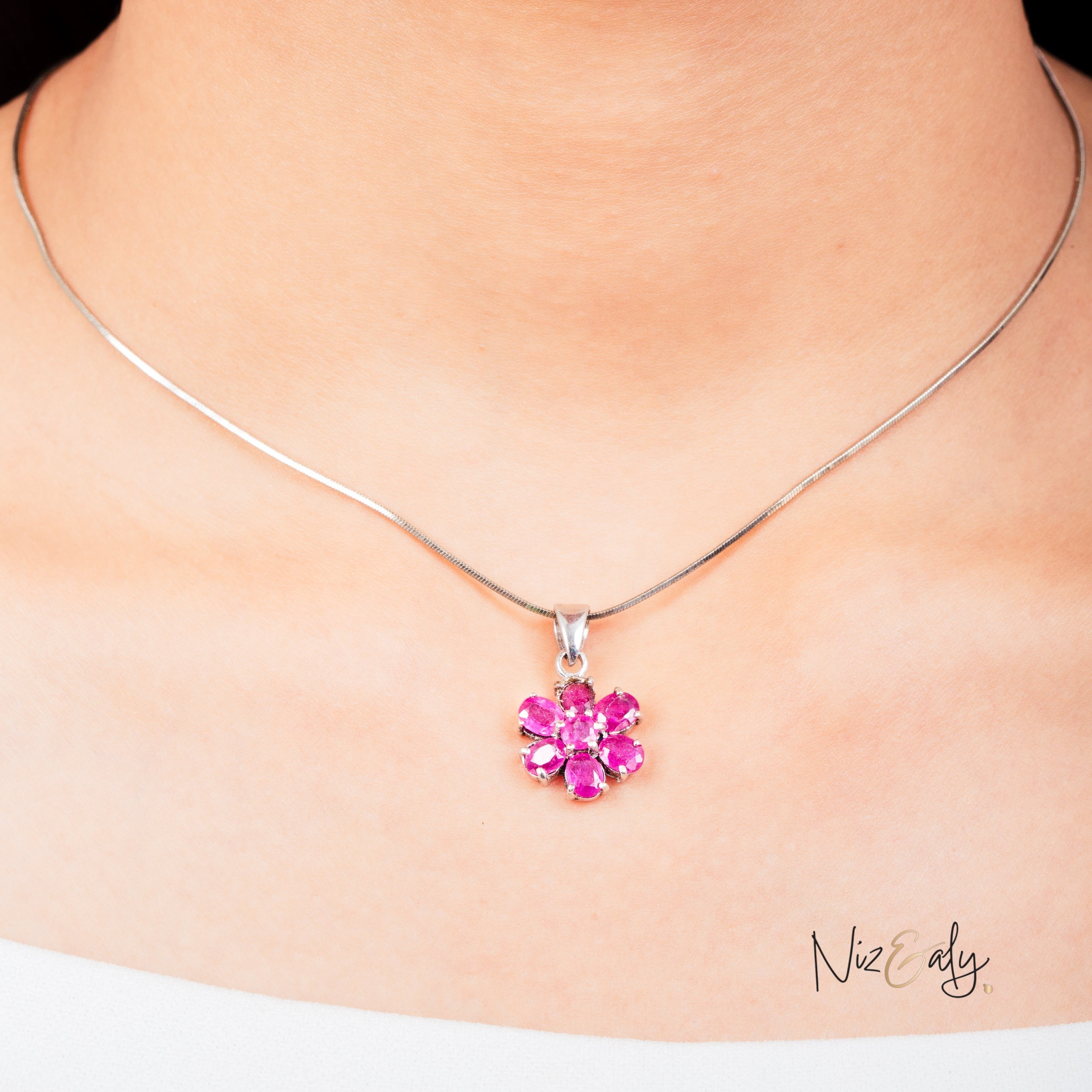 Niz & Aly ruby flower pendant featuring seven vibrant red rubies set in a delicate floral design on a silver chain