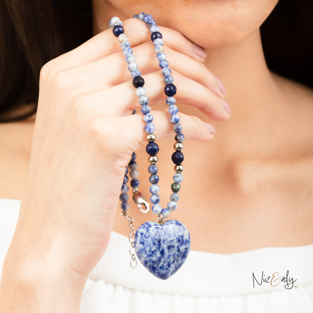 Niz & Aly sodalite heart pendant necklace with beaded Canadian blue stone strand worn by a woman in a white top.
