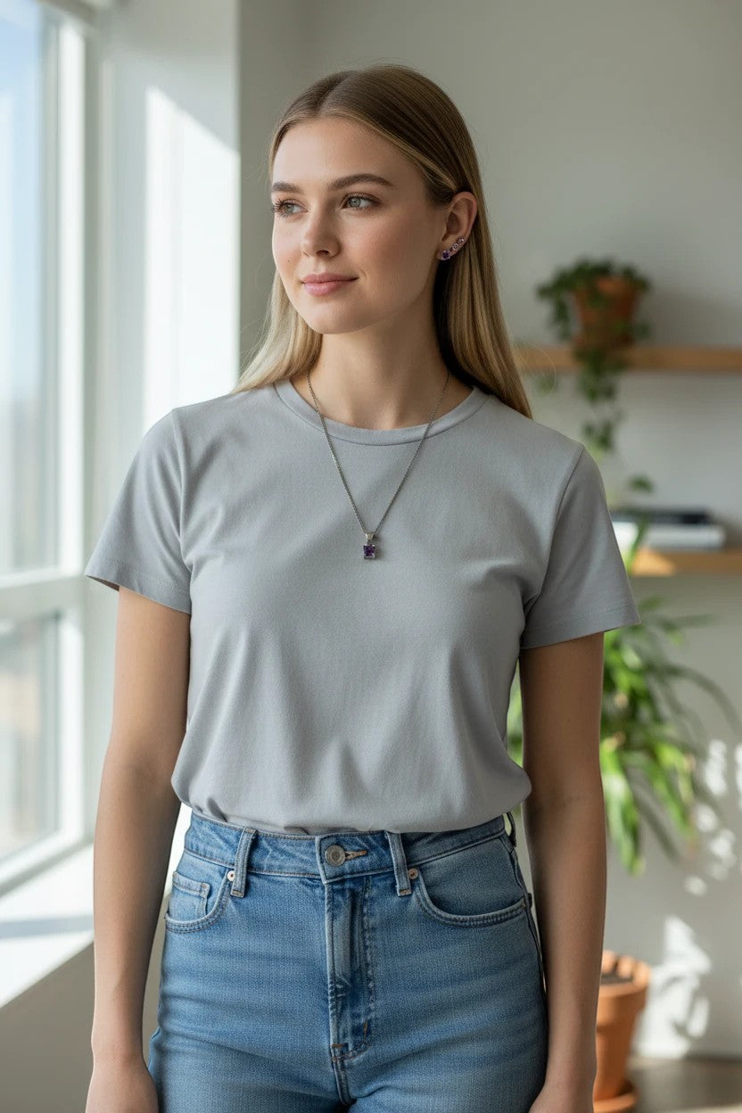 Niz & Aly dainty square amethyst necklace and earring set worn by a woman in a grey t-shirt near a window.