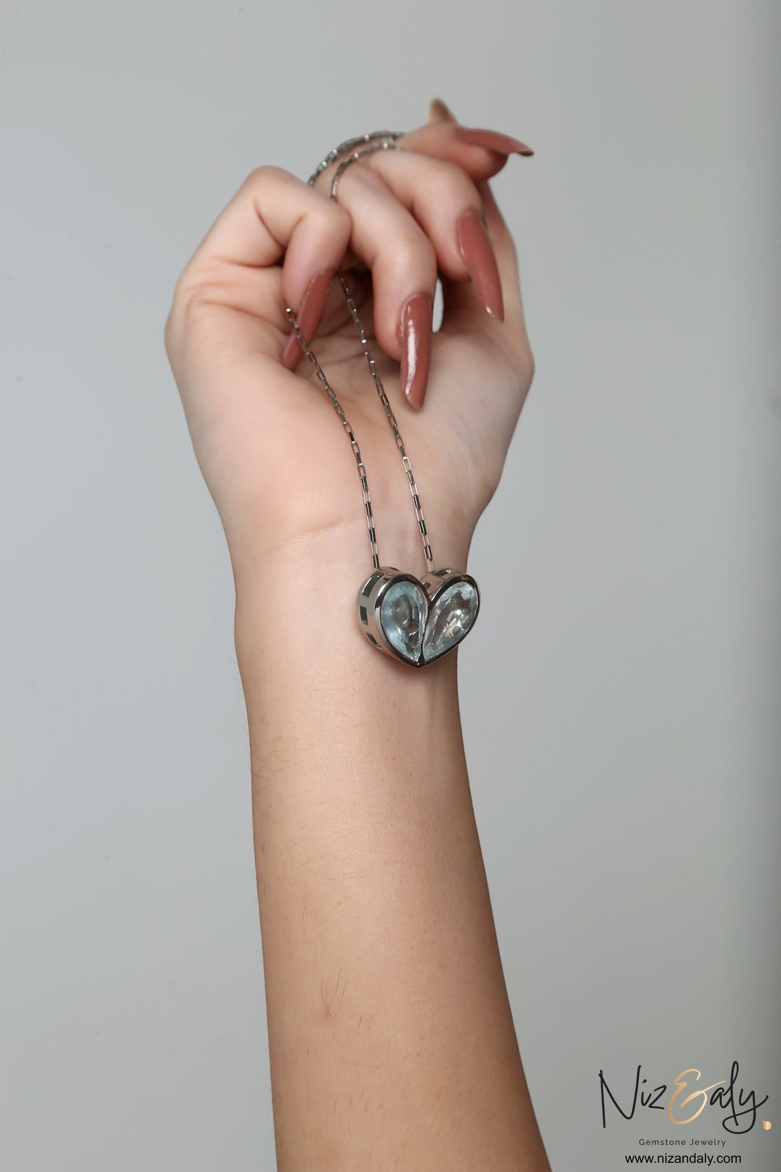 Niz & Aly sterling silver twin heart necklace featuring natural clear quartz crystals held in a hand