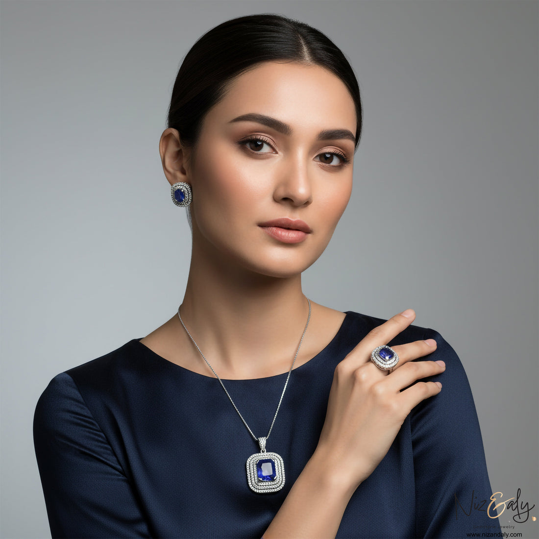 Niz & Aly tanzanite jewelry set featuring a pendant, earrings, and ring in sterling silver on a woman in navy blue