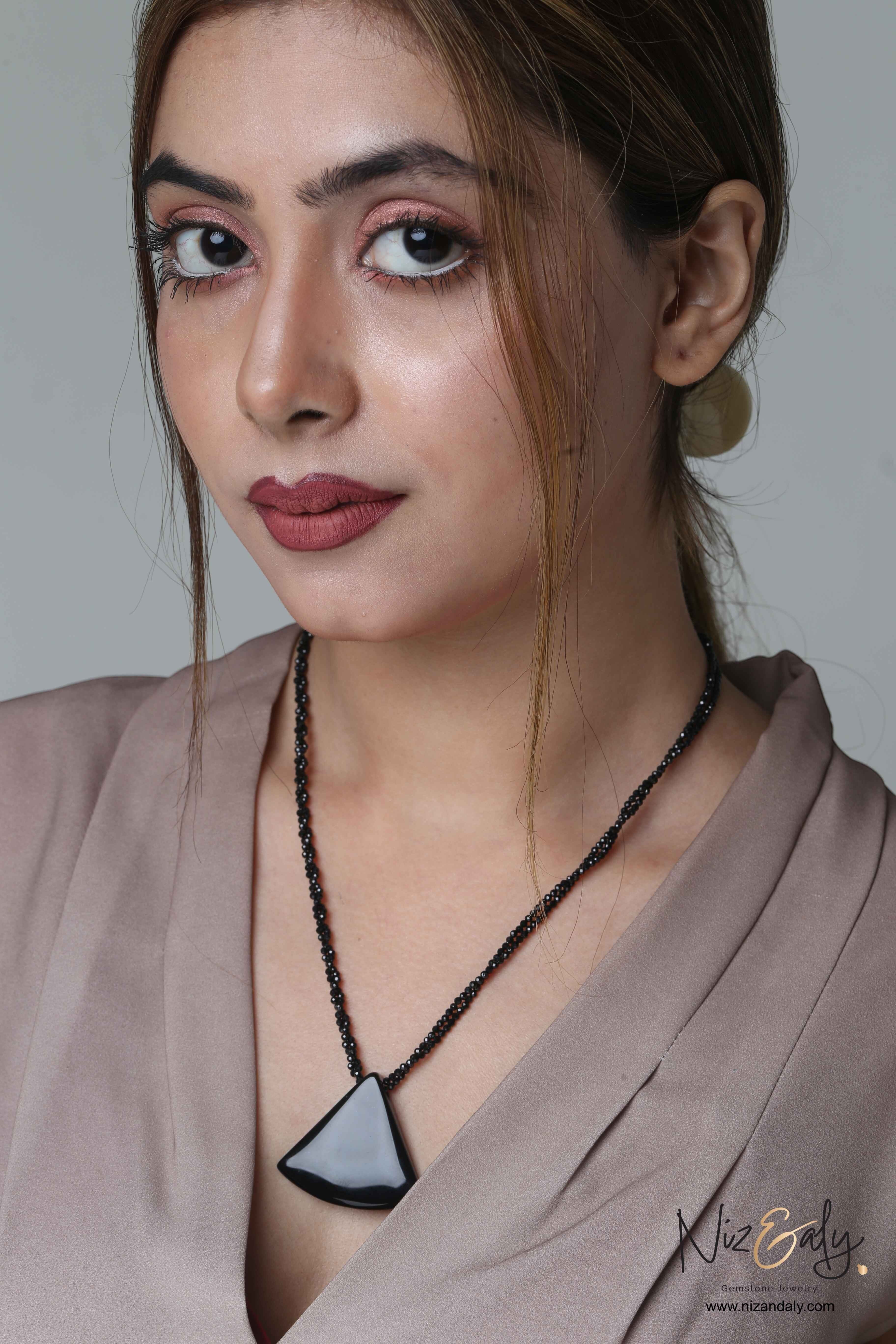 Niz & Aly Agate Eclipse necklace featuring a black triangular agate pendant on a twisted onyx beaded chain on a model