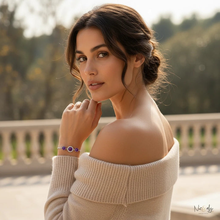 A woman wearing a Niz & Aly triple amethyst bracelet with faceted purple crystal beads on a soft beige off-shoulder top