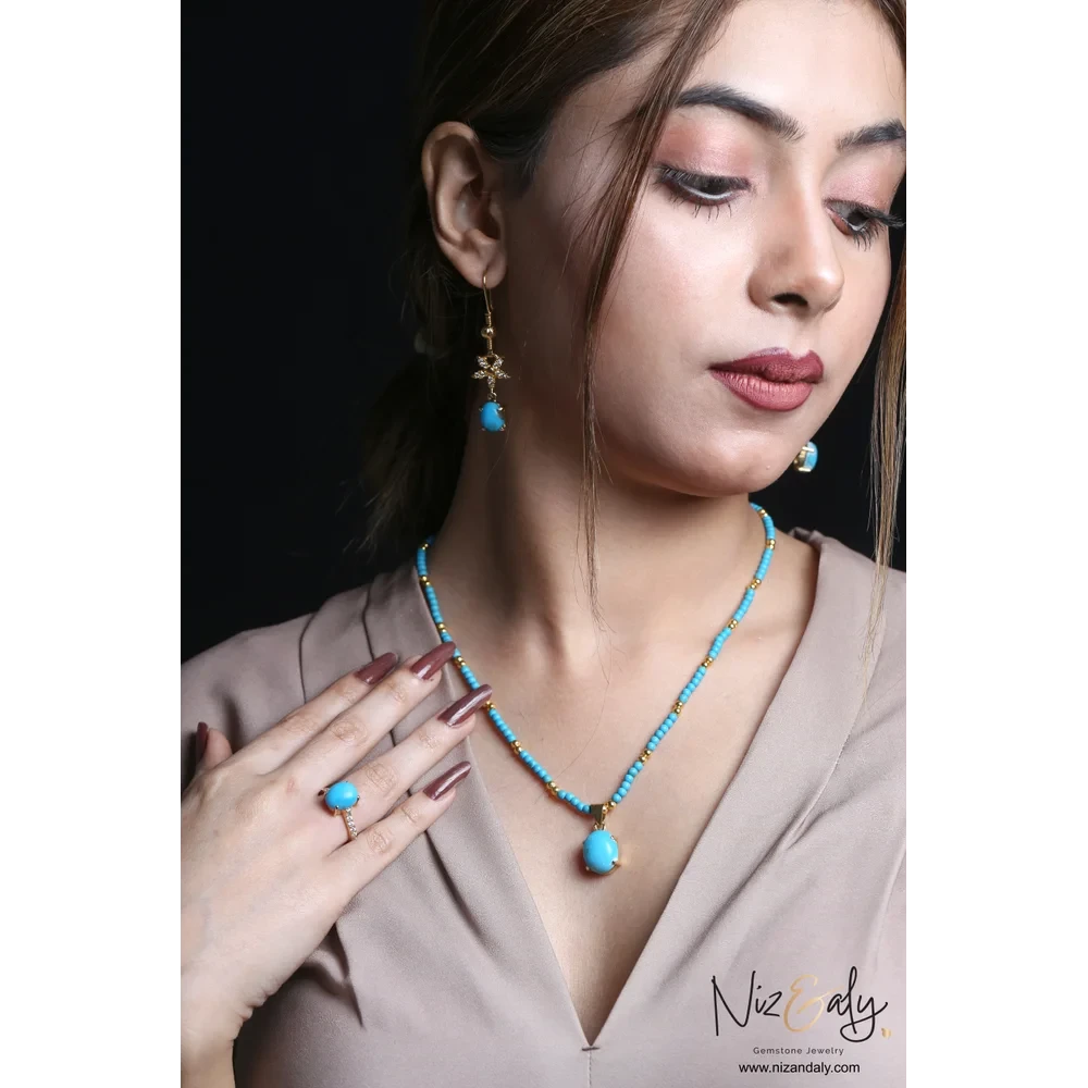 Niz & Aly turquoise gemstone necklace, drop earrings, and ring set with gold-tone accents worn by a woman.