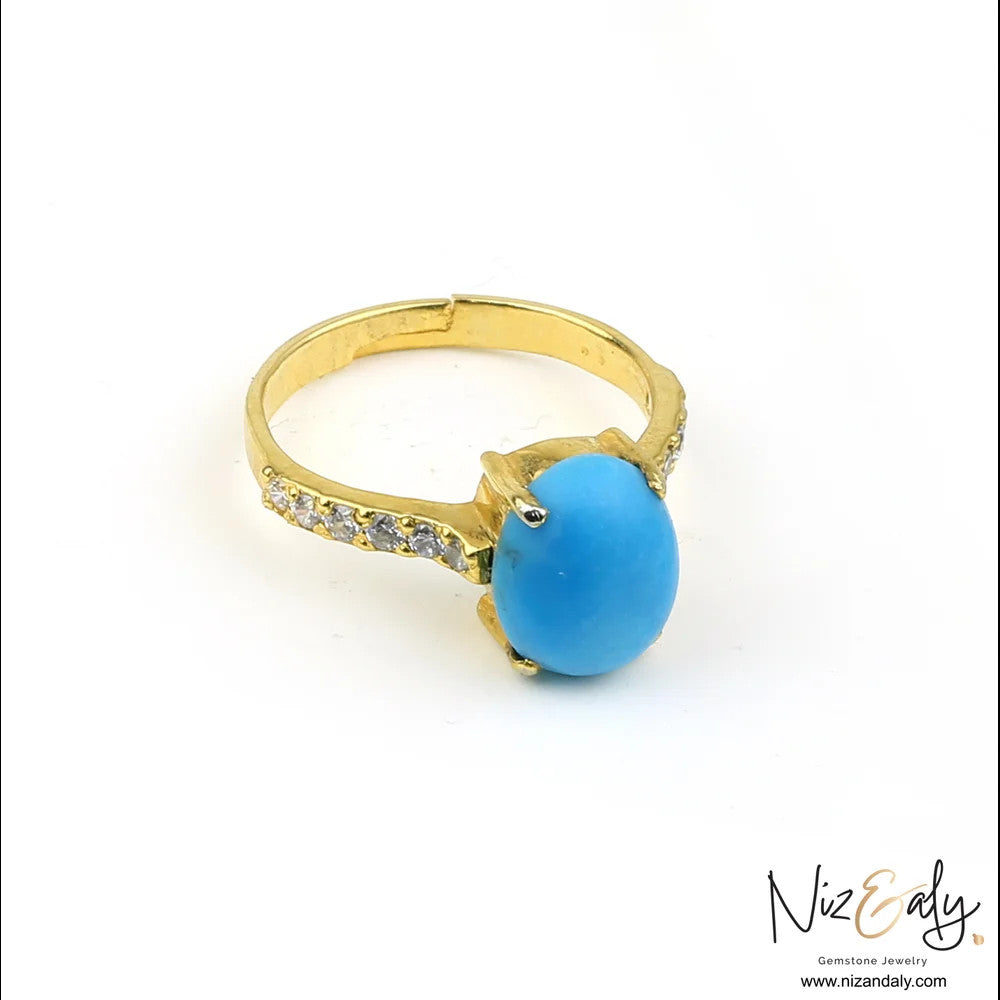 Niz & Aly gold-tone ring featuring a smooth oval turquoise gemstone and sparkling crystal accents on the band.