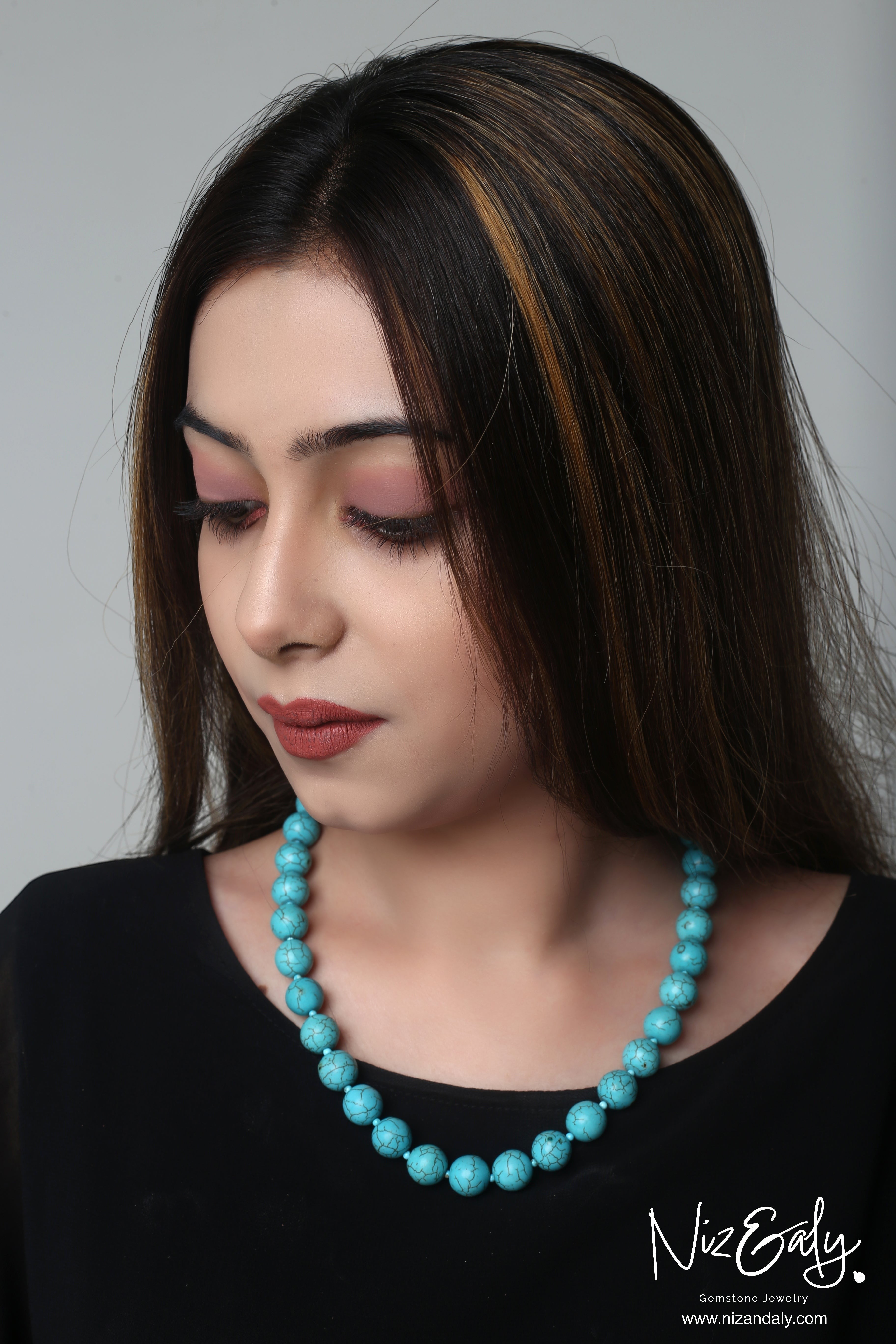 Niz & Aly turquoise howlite beaded necklace worn by a woman with long dark hair against a neutral background.