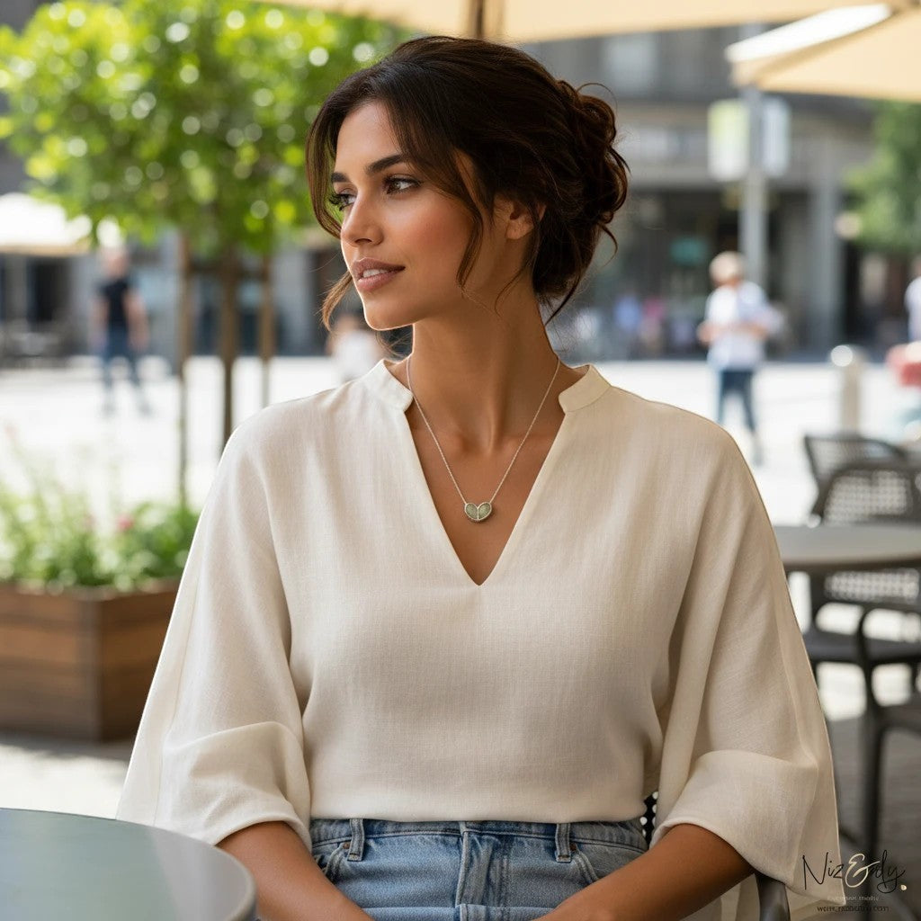 Niz & Aly twin heart prehnite pendant necklace worn by a woman in a white blouse at an outdoor cafe