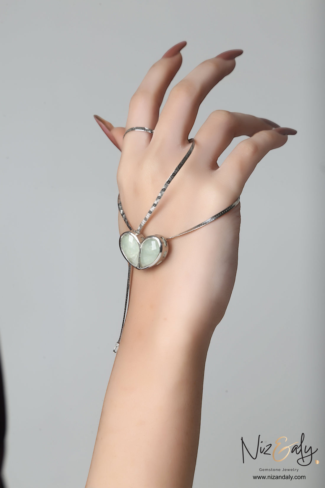 Niz & Aly twin heart prehnite pendant necklace on a silver chain worn on a hand against a neutral background.